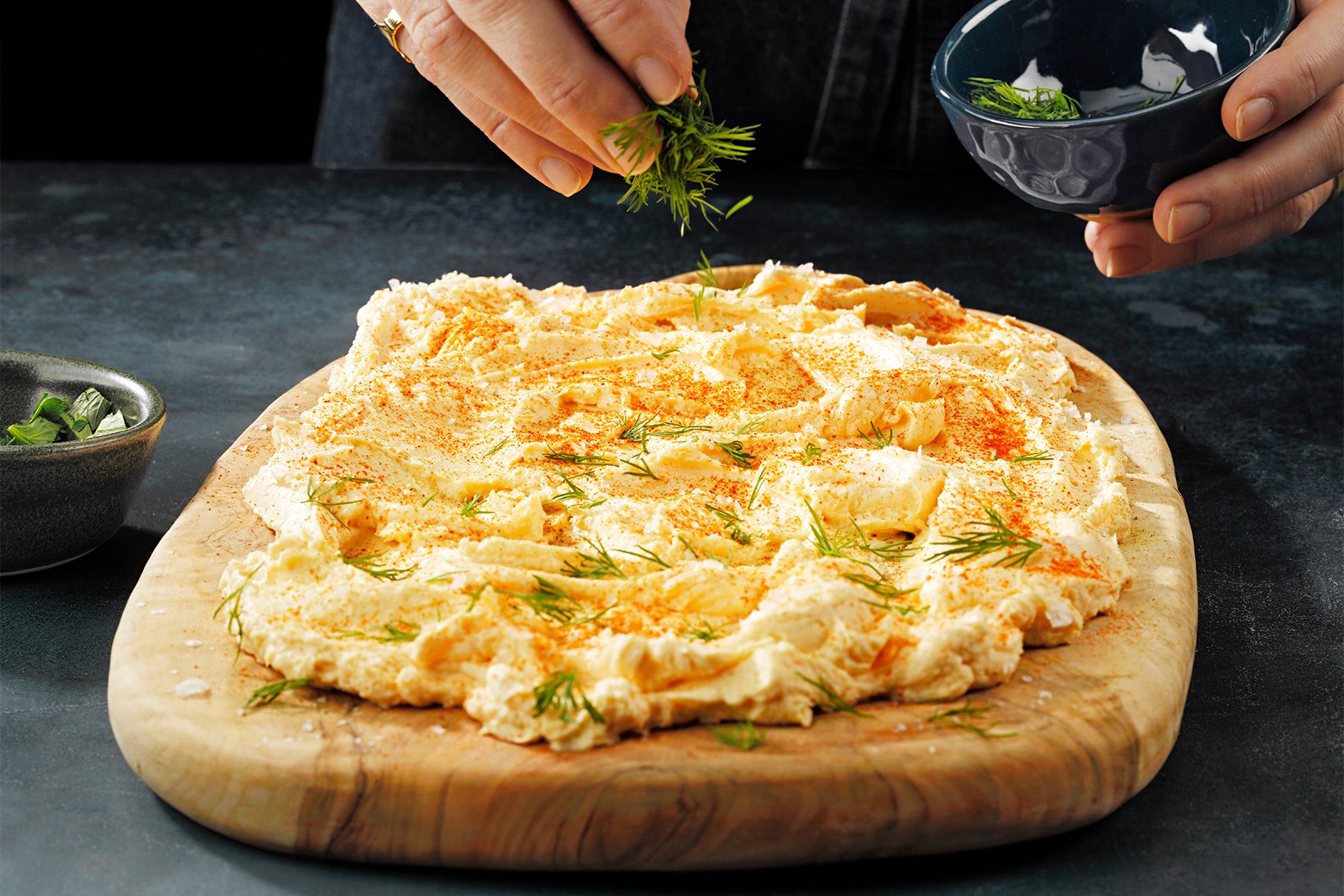 A person sprinkling greens on a wooden board 