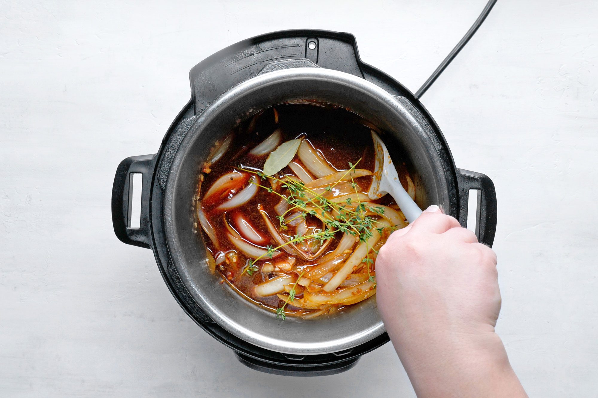 overhead shot; white background; Stir in beef broth, wine, thyme and bay leaf in pressure cooker;