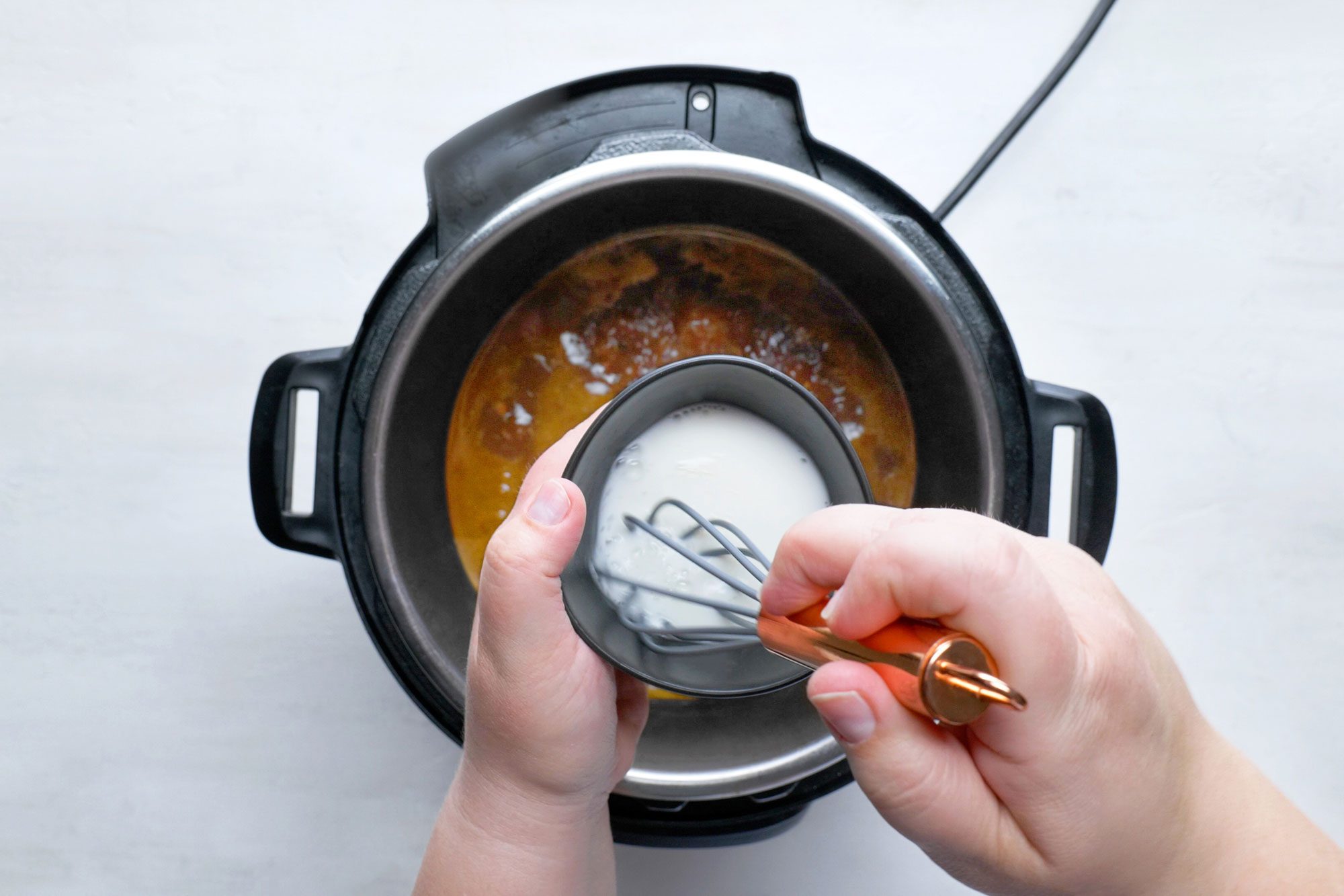 overhead shot; white background; adding cornstrach to the dish in pressure cooker;