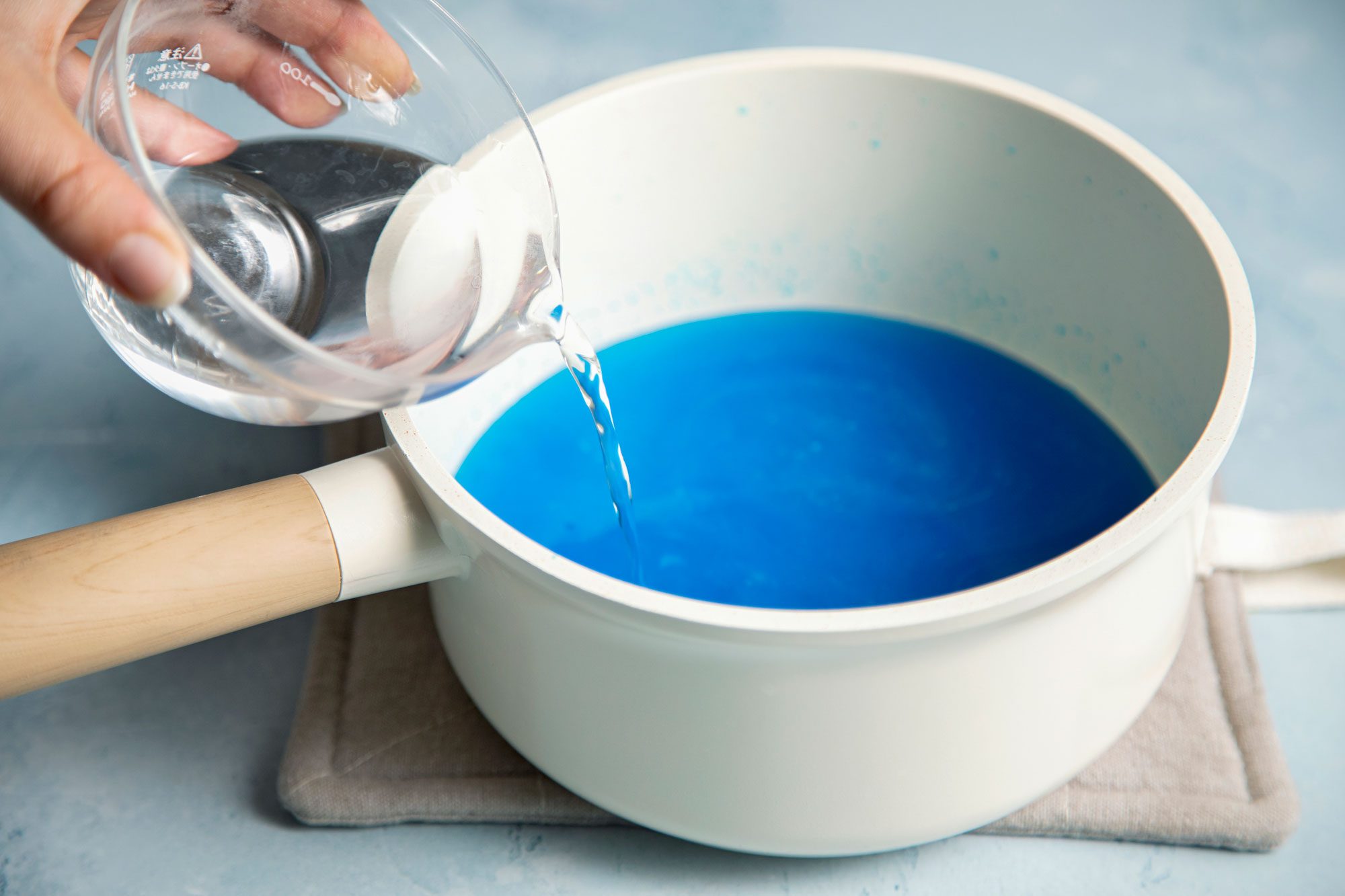 wide shot of vodka added in the berry blue gelatin mix in a sauce pan