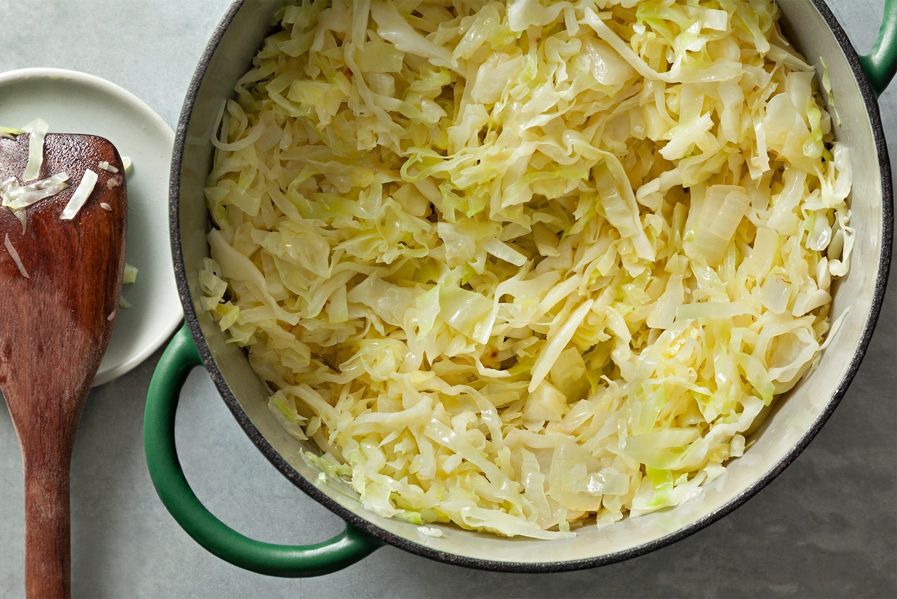 A green frying pan with a wooden handle is filled with browned ground beef.