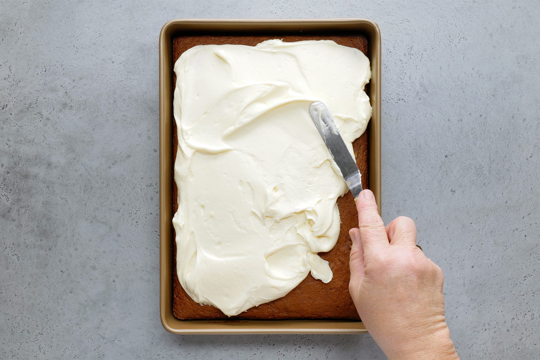 spreading frosting cream over baked pumpkin pecan cake
