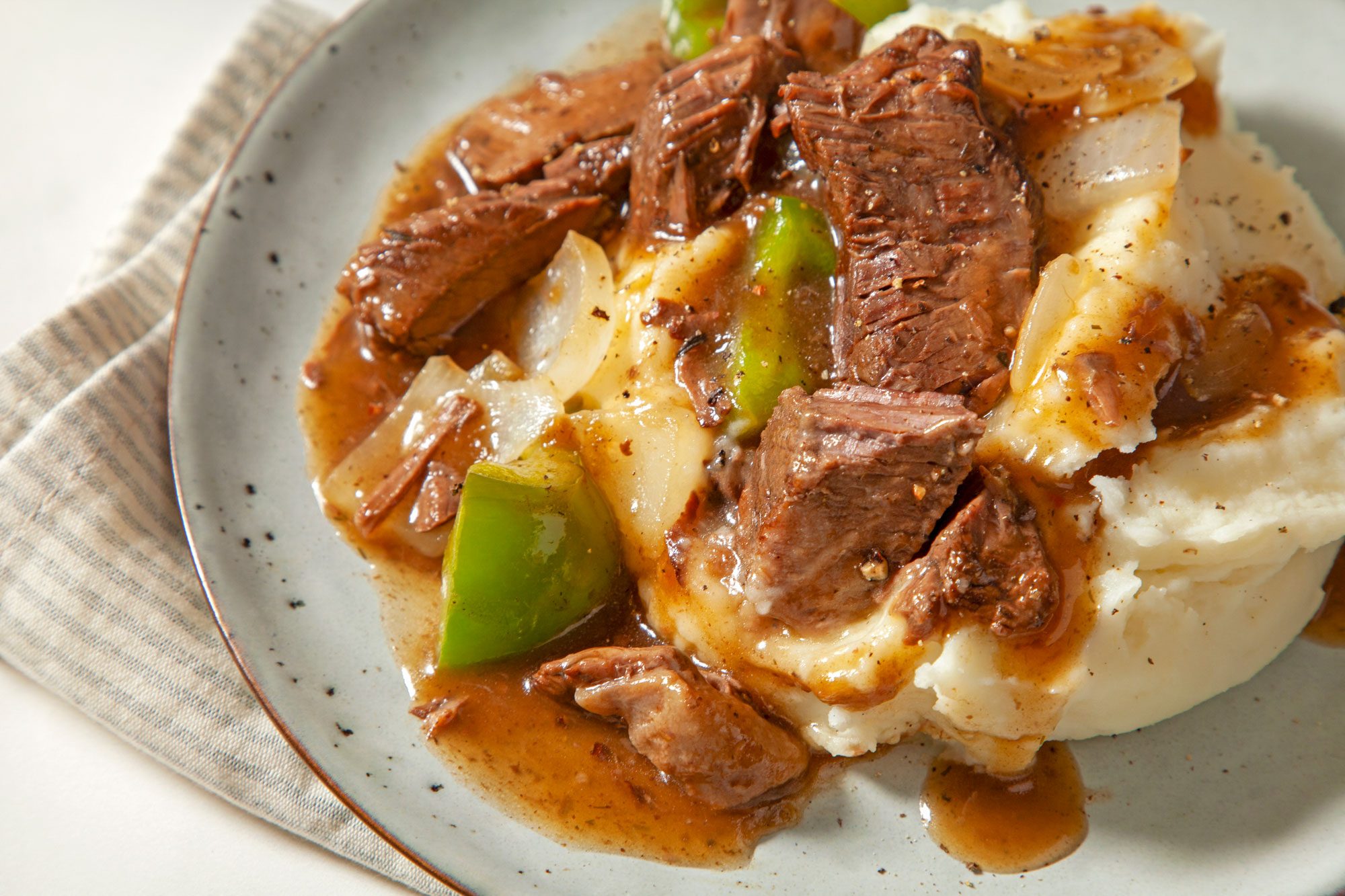 Close shot of Slow-Cooked Sirloin; served on ceramic plate; napkin; cream marble background;