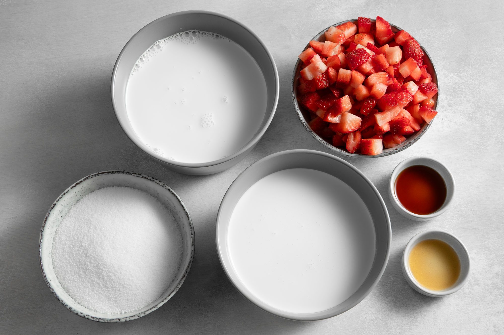 Overhead shot of all ingredients for Strawberry Ice Cream on white marble background