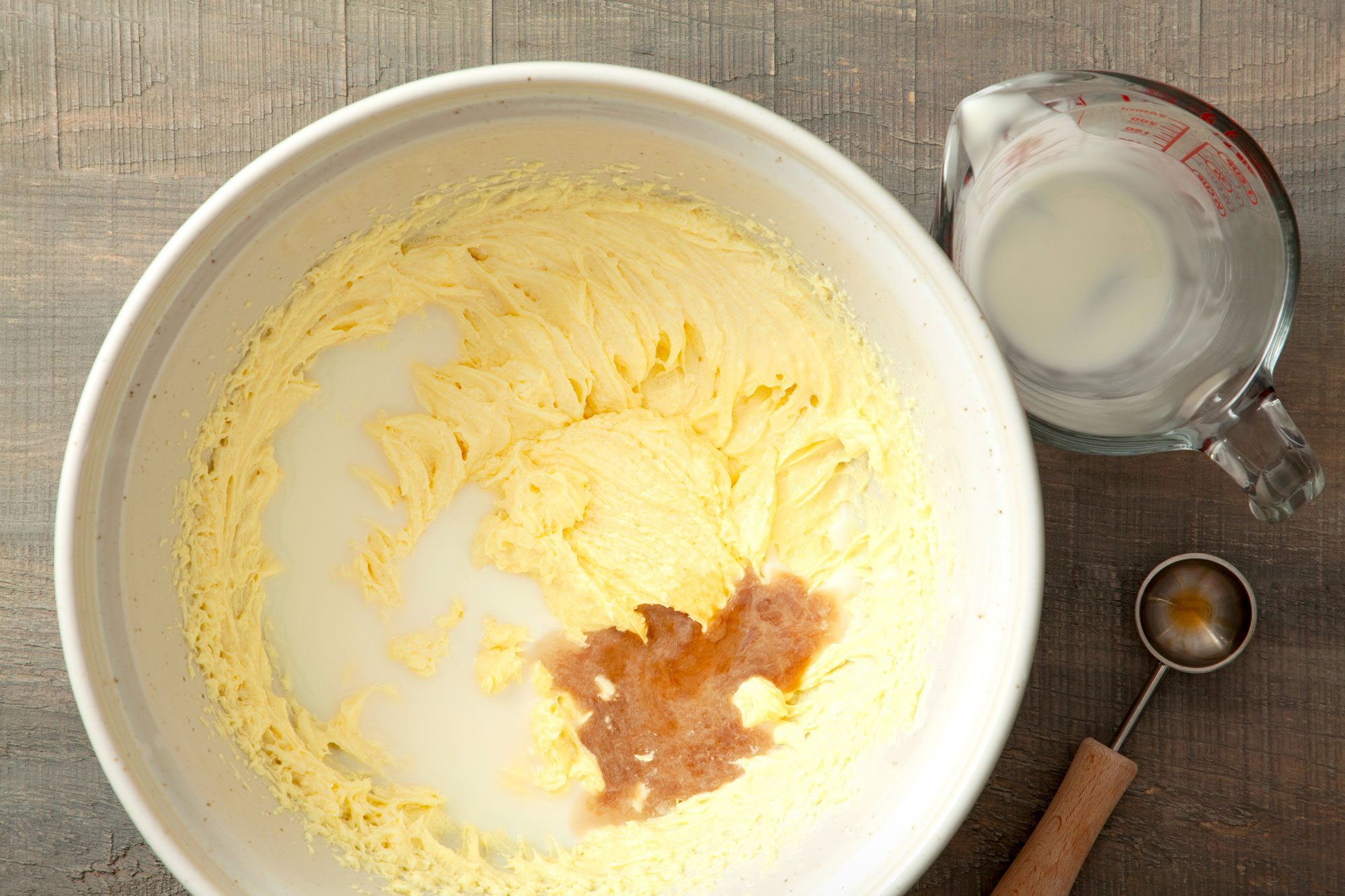 milk, vanilla extract and butter-sugar mixture in a large bowl on a wooden surface