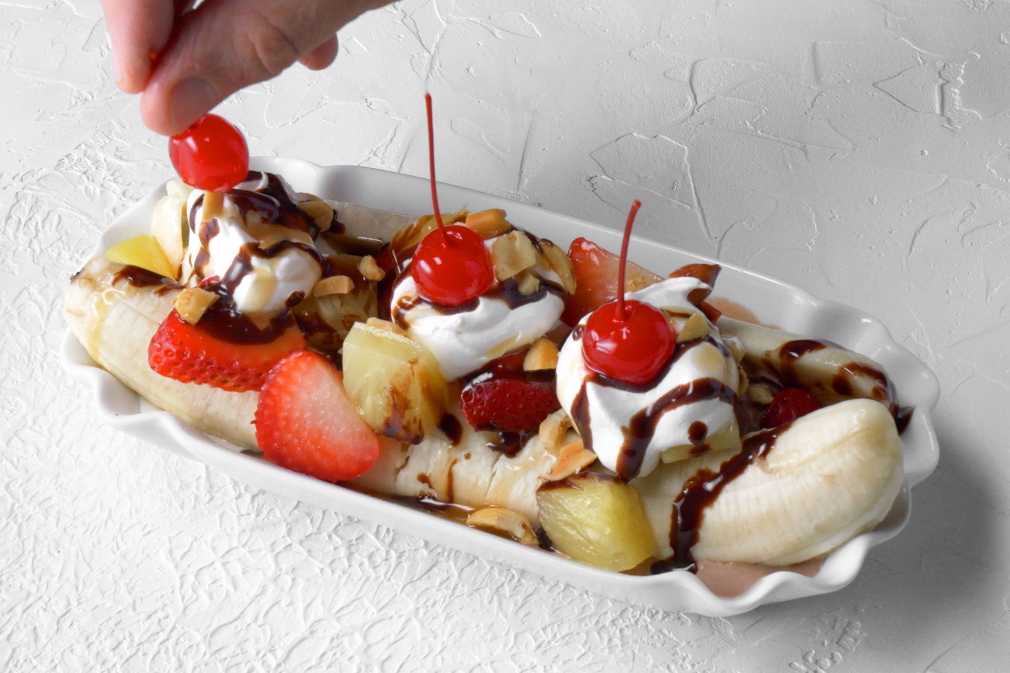 3/4th shot; white background; garnishing banana split with red cherries;