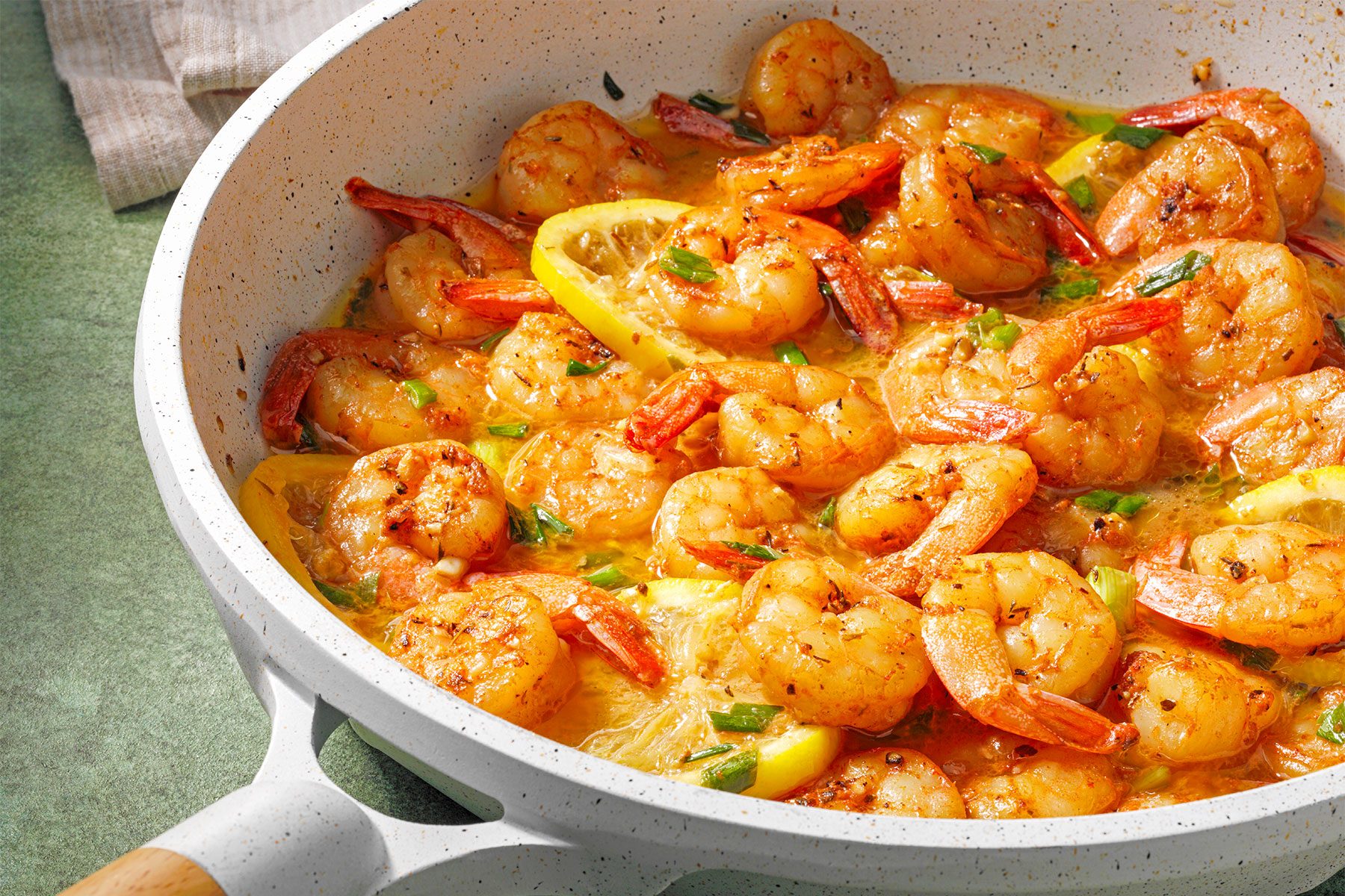 Close shot of Barbecue Shrimp; served on white ceramic plate; with bread; sprinkled with parsley over top; chopping board; lime slices; green texture background;