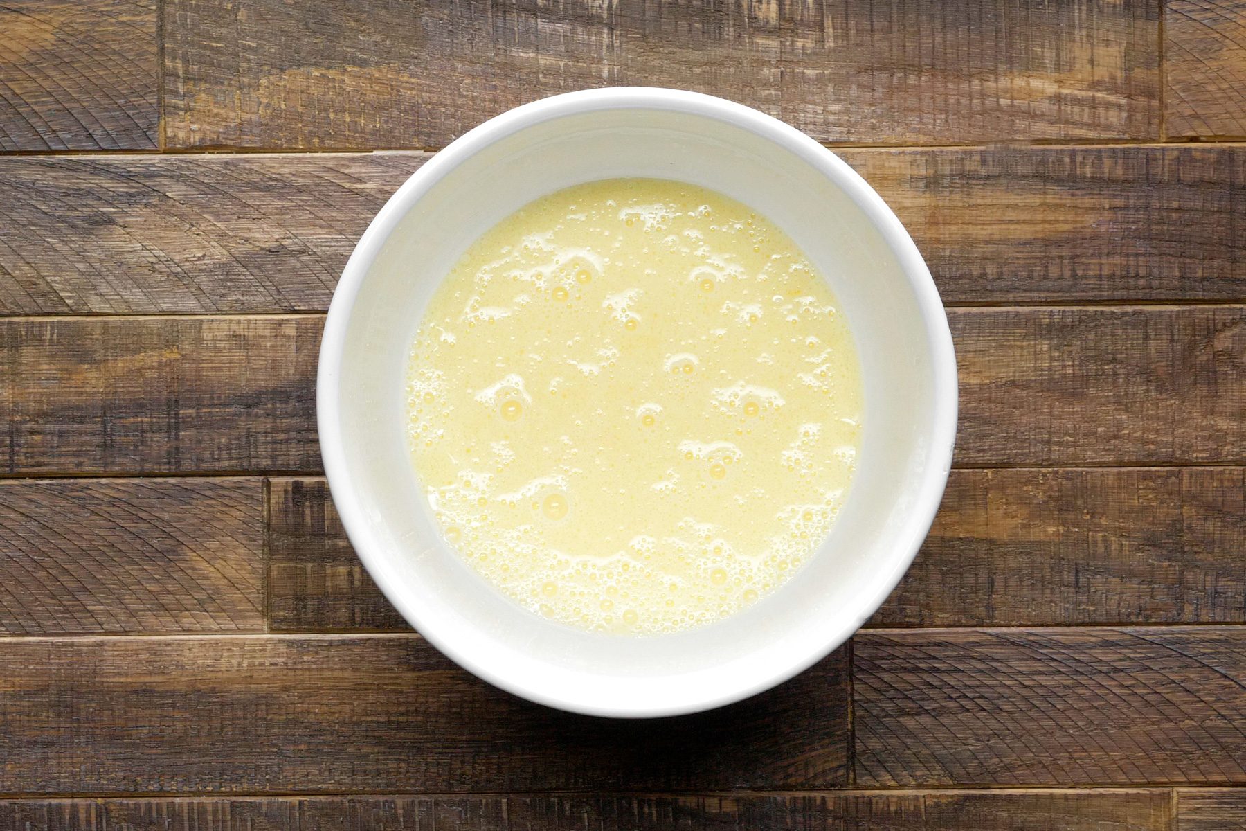 A white bowl of a mixture of egg, milk, and oil.