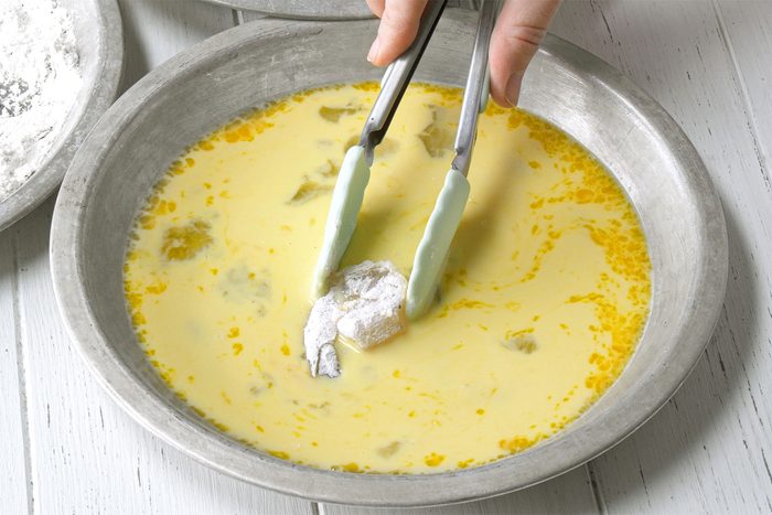 3/4 angle view shot of dip in egg mixture; with the help of tongs; white wooden background;
