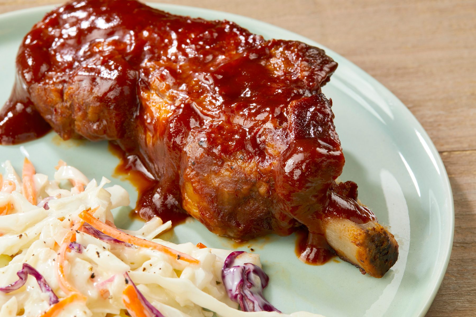 A plate of country Ribs in The Oven served with corn on the cob and a side of chopped salad