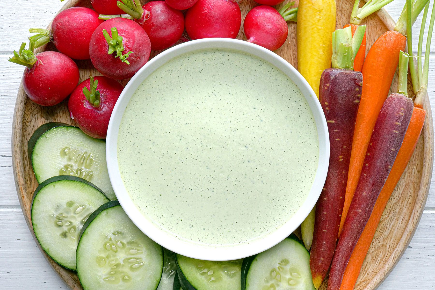 Overhead shot of Green Goddness Dressing; served with salad; wood plate; white wooden background;