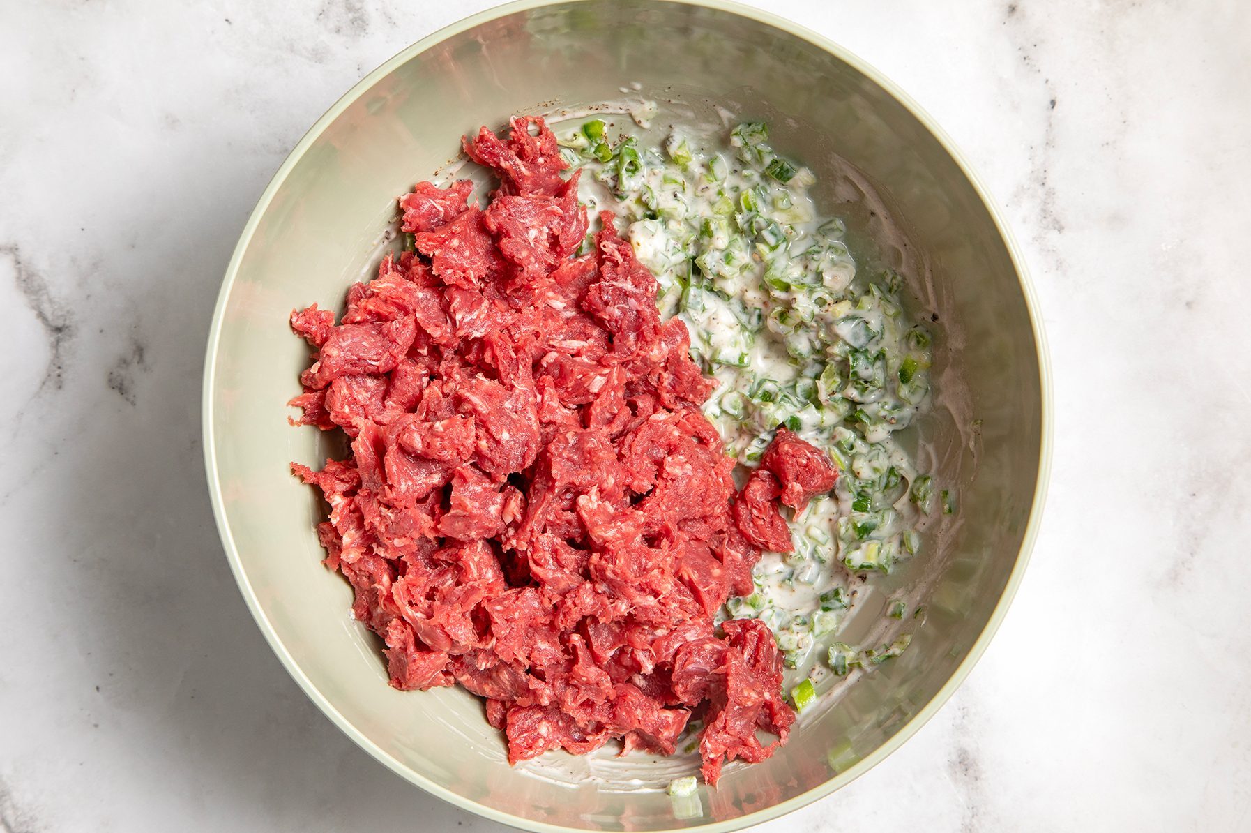 A green bowl on a marble surface contains a mixture of ingredients. 