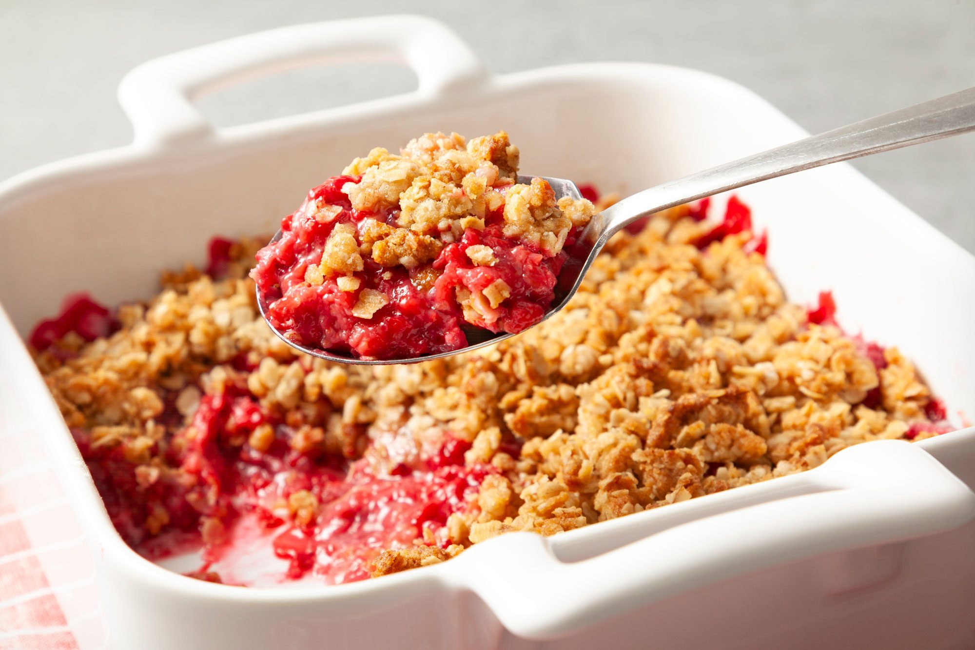 3/4th shot; white background; Raspberry Crisp in a square baking dish; Raspberry Crisp on a silver spoon;