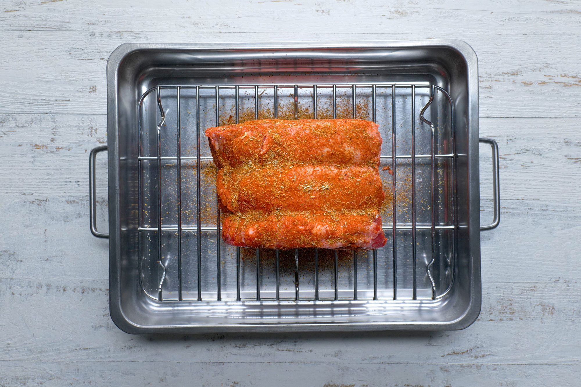 Top view shot of place roast on a rack in a roasting pan; fat side up; rub with seasonings; roast uncovered; white wooden background;
