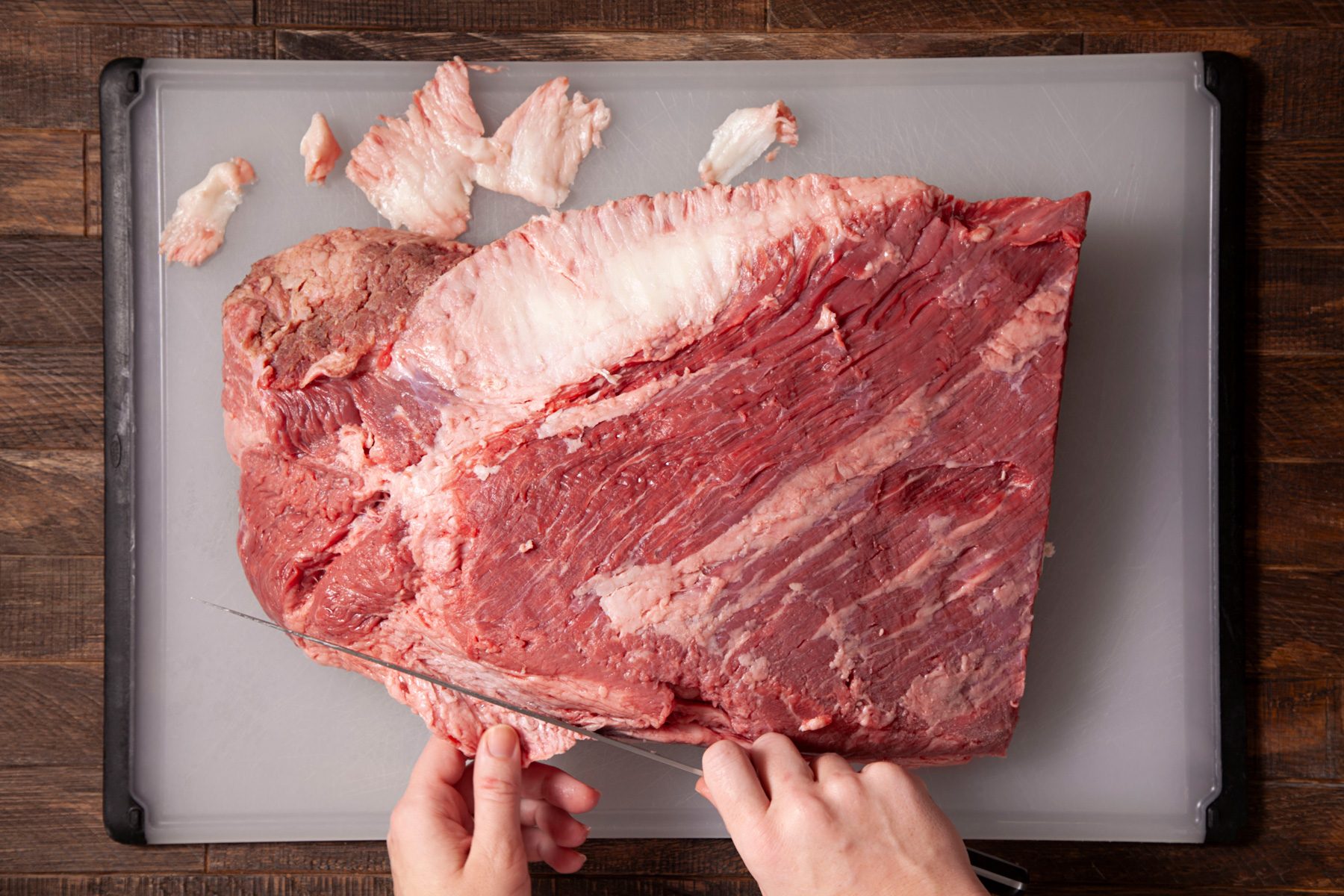 A person cutting sides of brisket on a cutting board