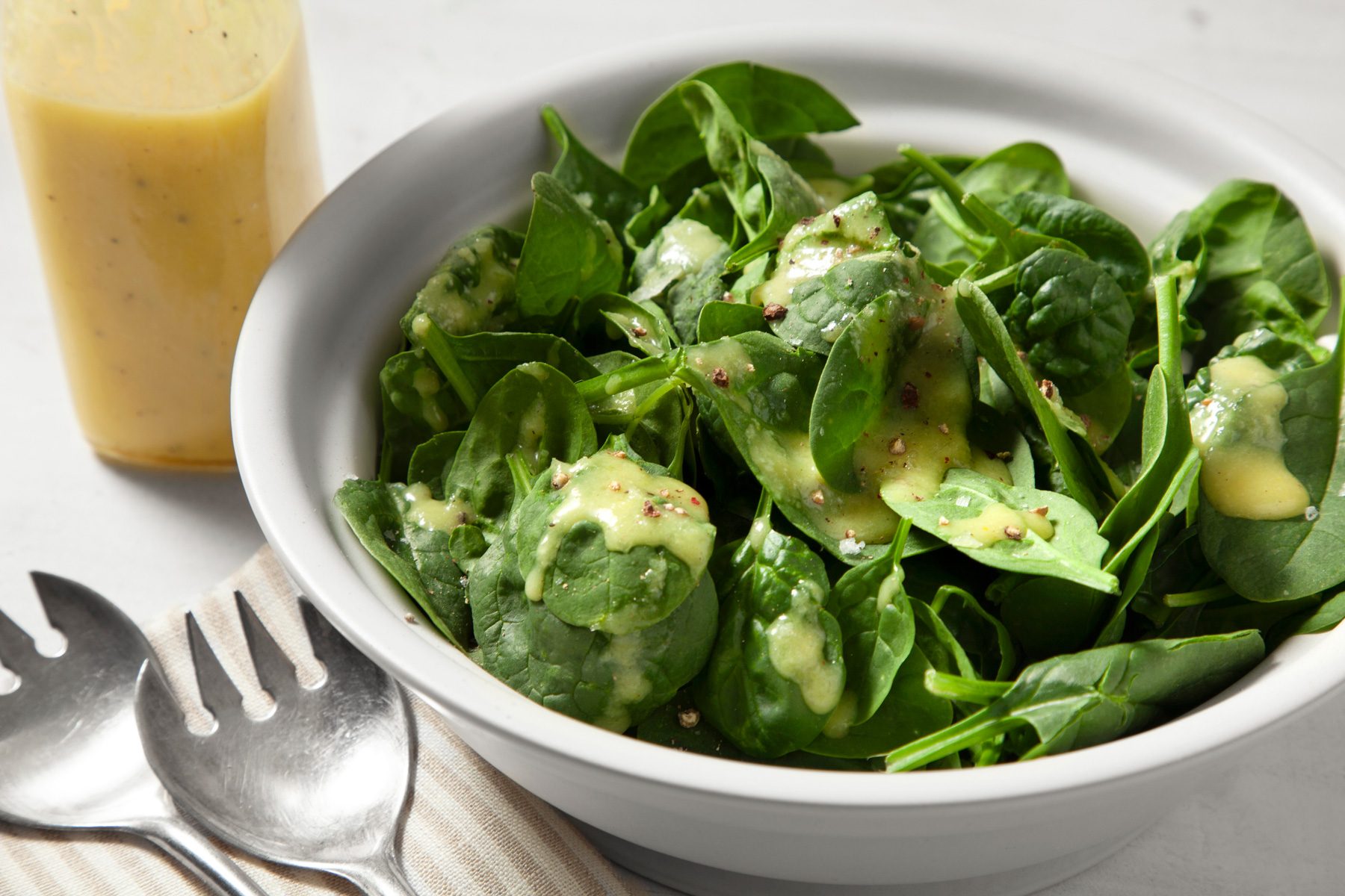 Close up image of Spinach Salad Dressing sprinkled on spinach salad in a bowl