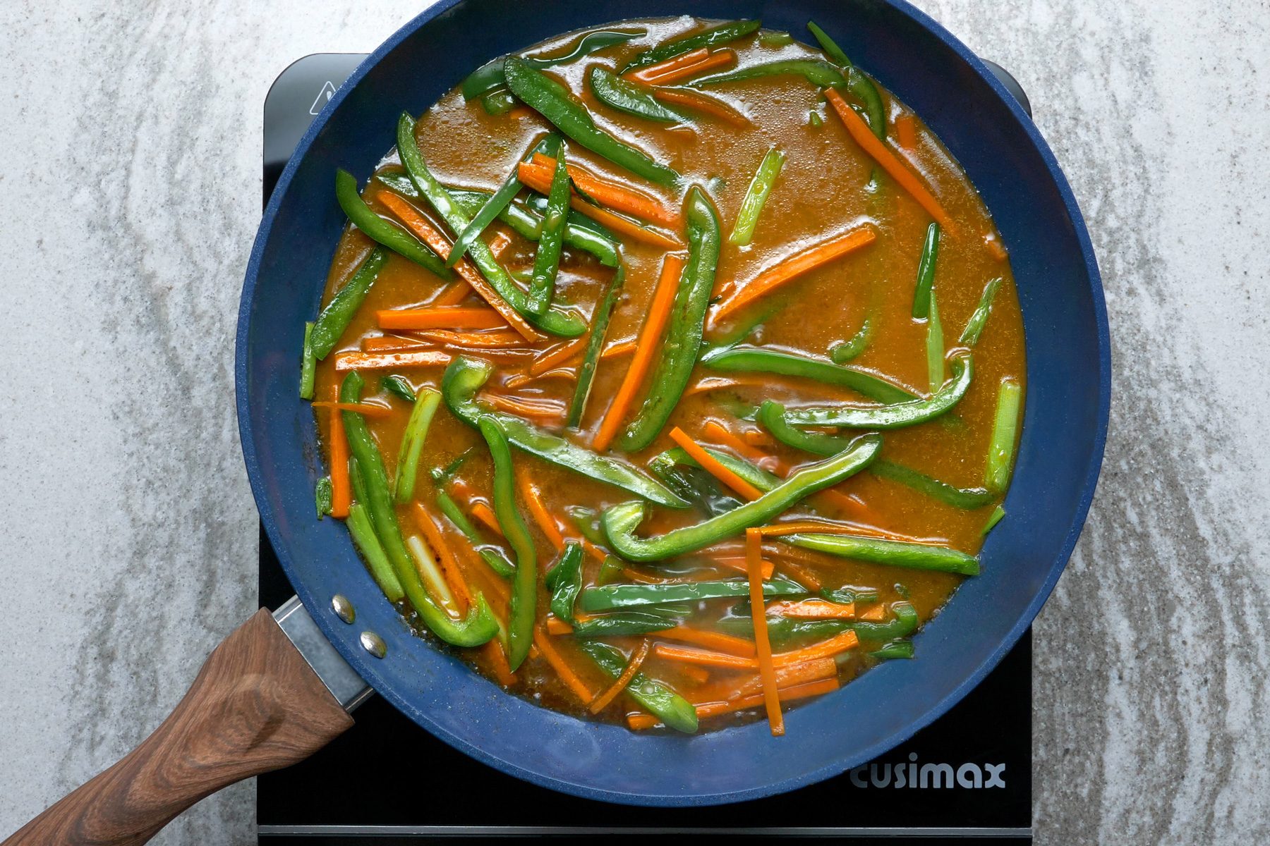 Sliced vegetables are boiling in a soy sauce mixture in a wok.