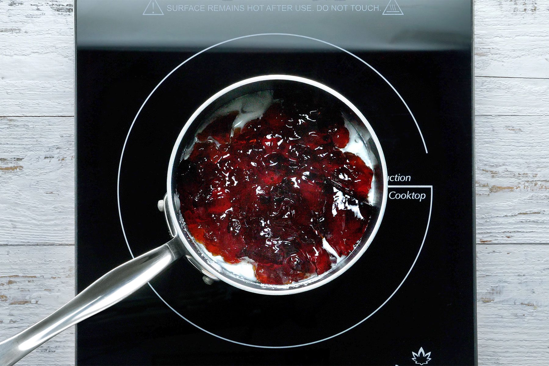 Overhead shot of a saucepan; combined cornstarch and water until smooth; add jelly and cook; stirring constantly until jelly is melted and mixture has thickened; wooden background;