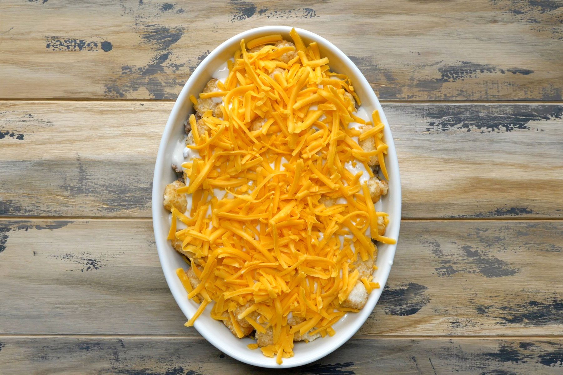 Overhead shot of baking pan; combined soup and milk; pour over potatoes; sprinkle with cheese; and bake; wooden background;