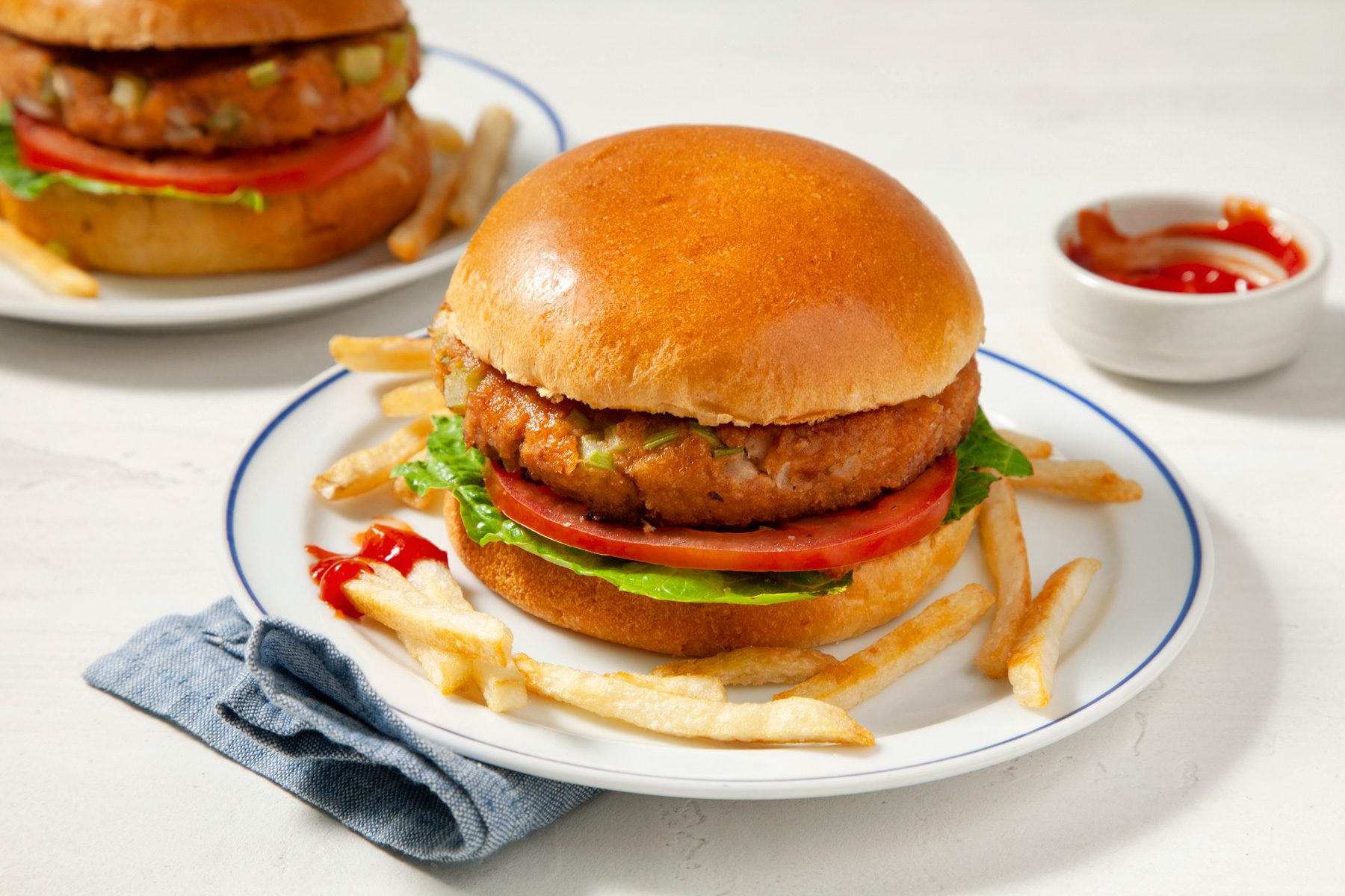 Two plates of tuna burgers served with French fries and sauce