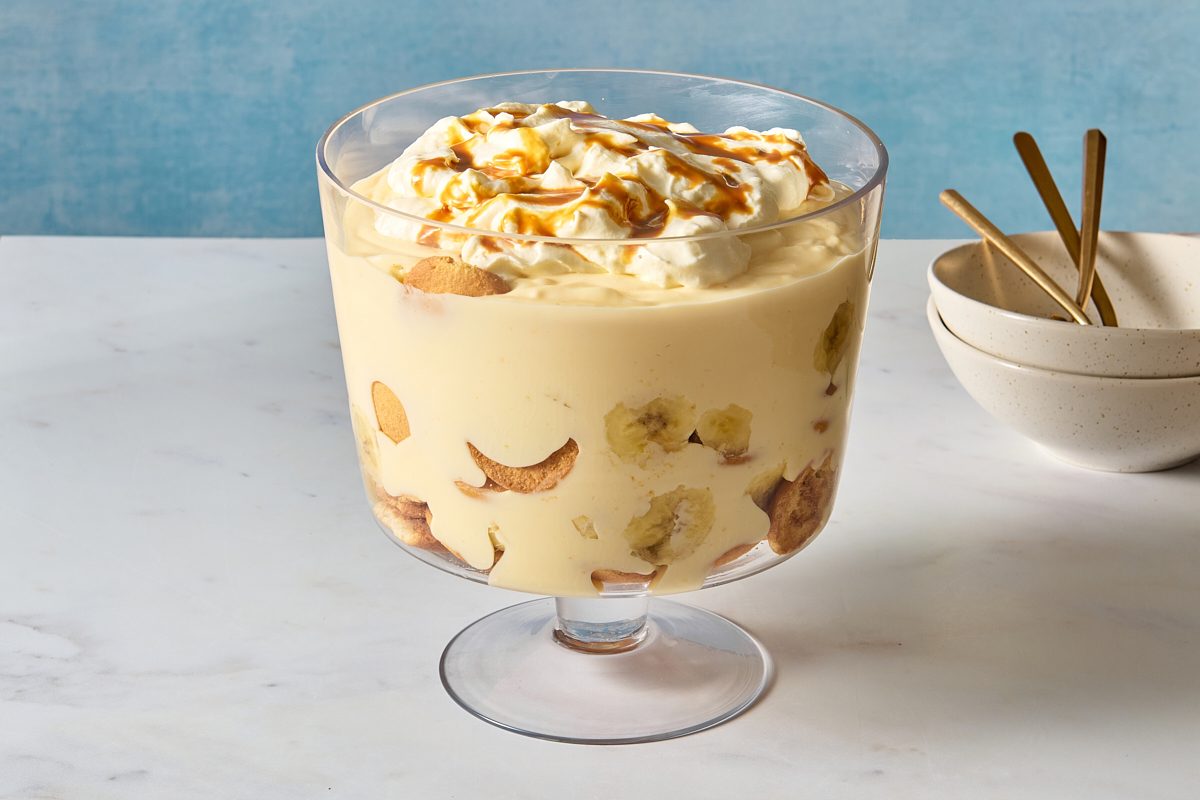 Banana pudding cup in a large glass dish, topped with whipped cream and caramel sauce