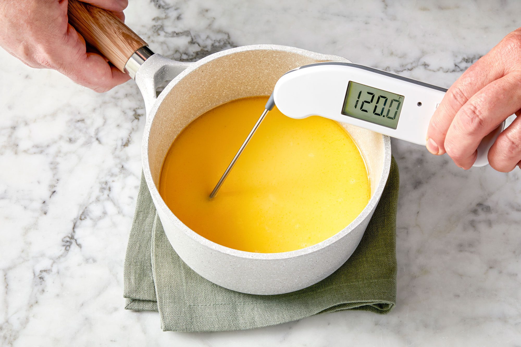 wide shot of digital thermometer reading temperature of a yellow liquid in a white saucepan