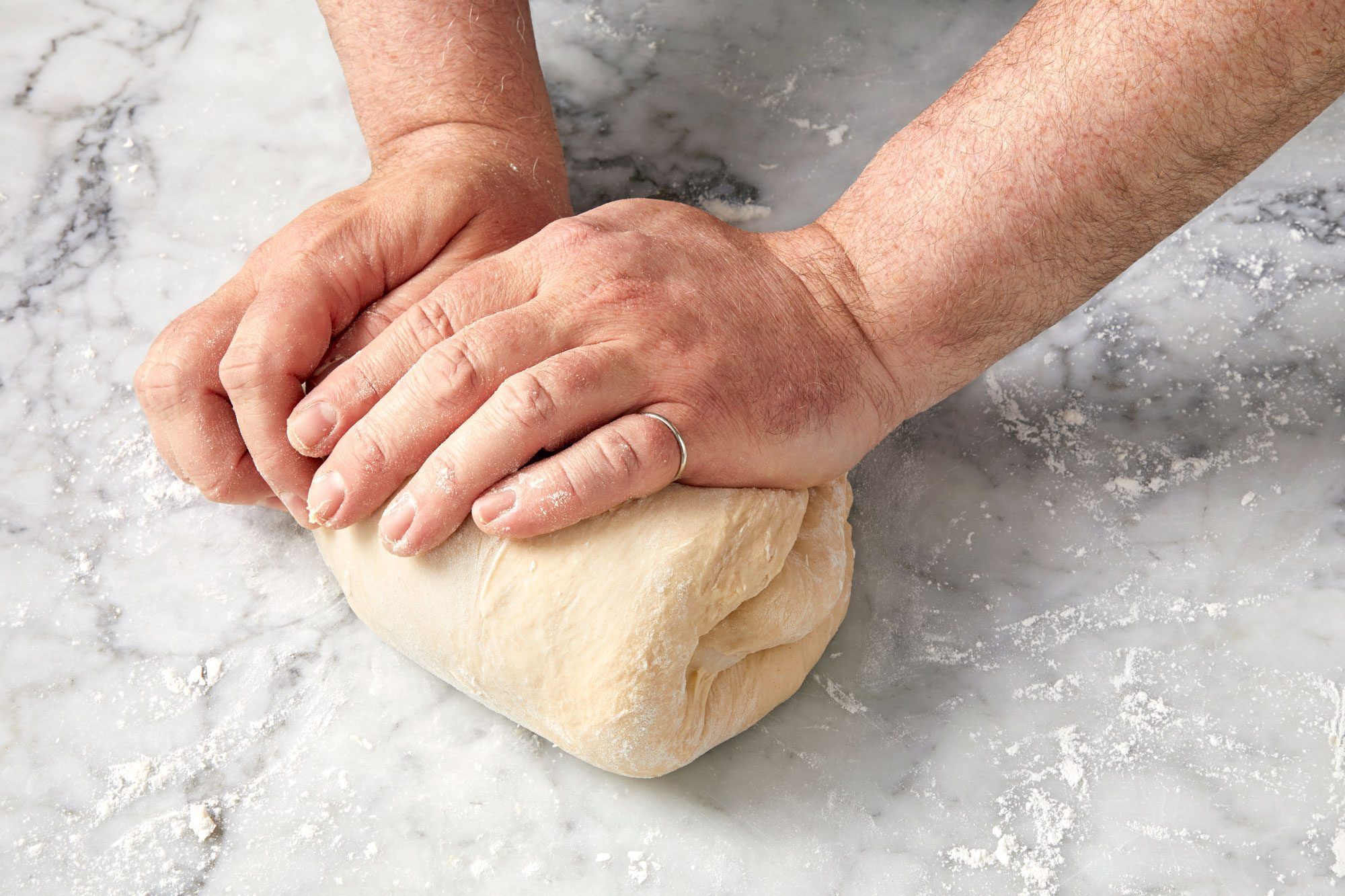 wide shot of hands kneading dough; marble surface;