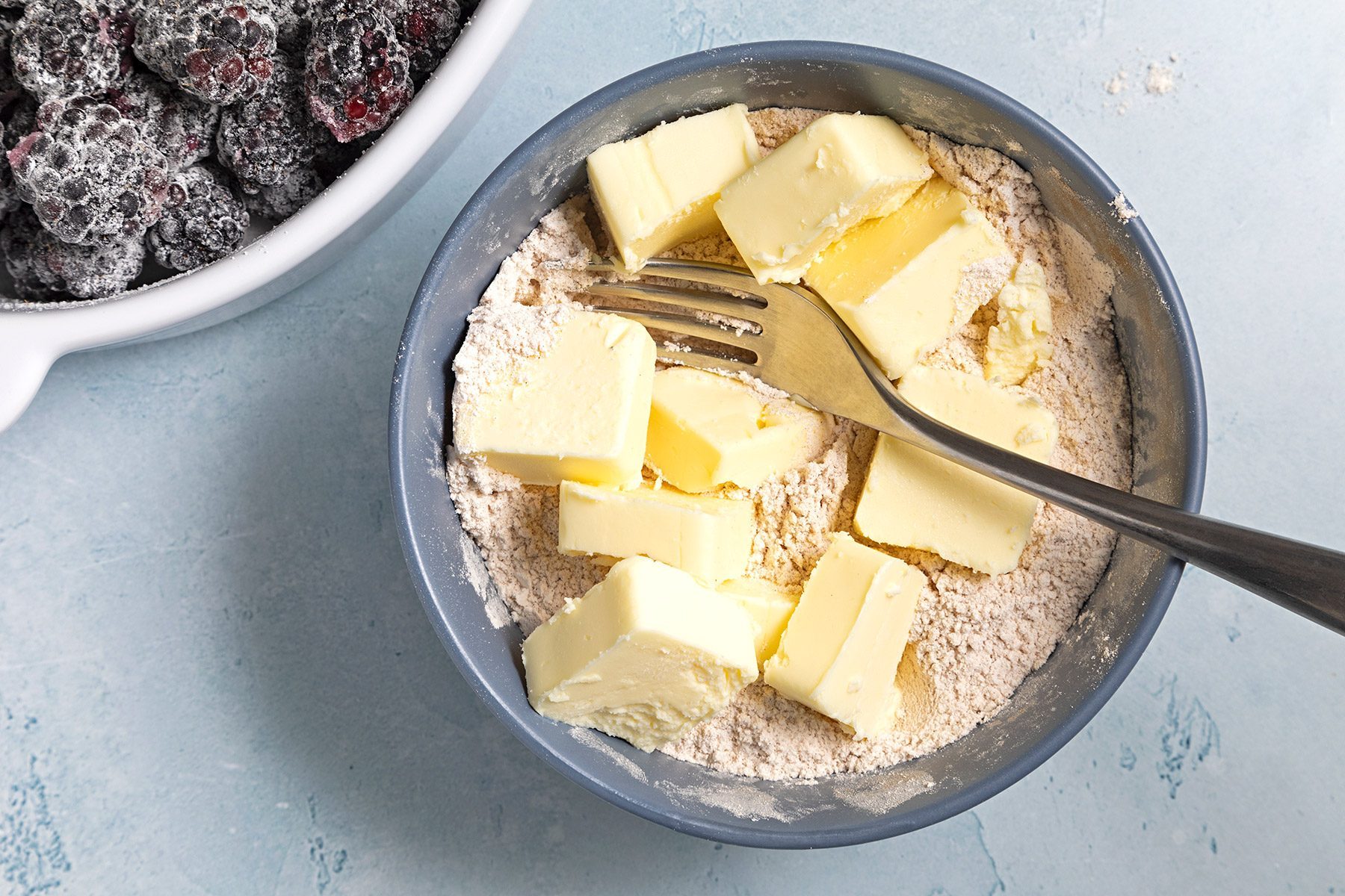 Overhead shot of cut butter in cubes add in mixture; fork; blue marble background