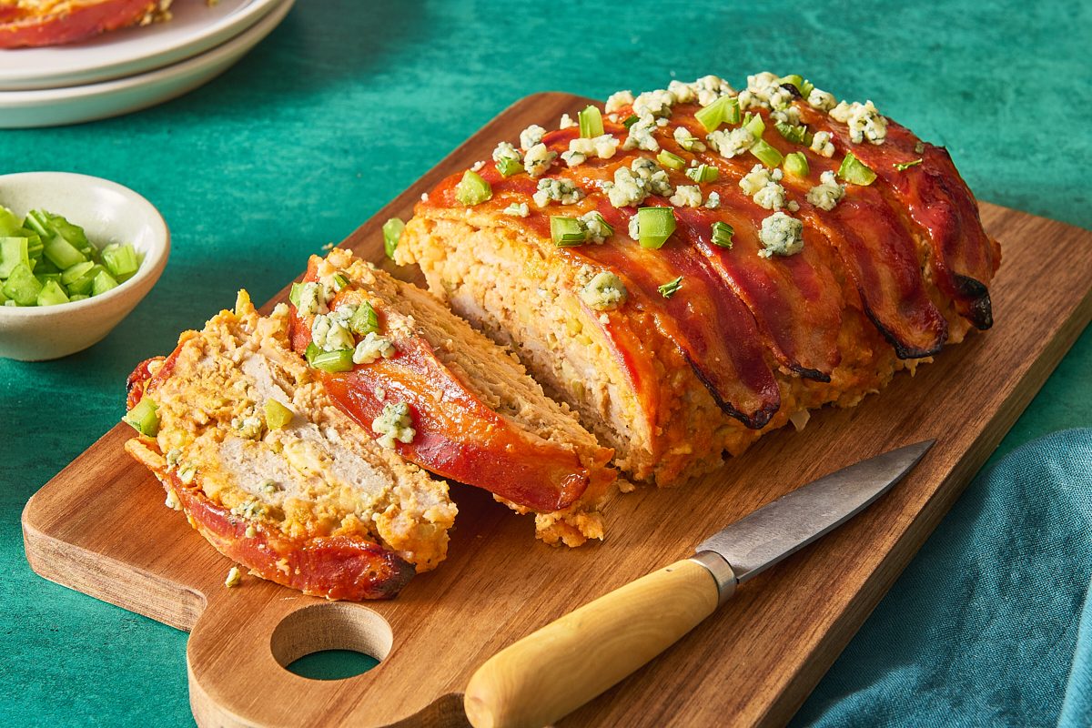 Angled shot of buffalo chicken meatloaf partially cut into slices on a cutting board