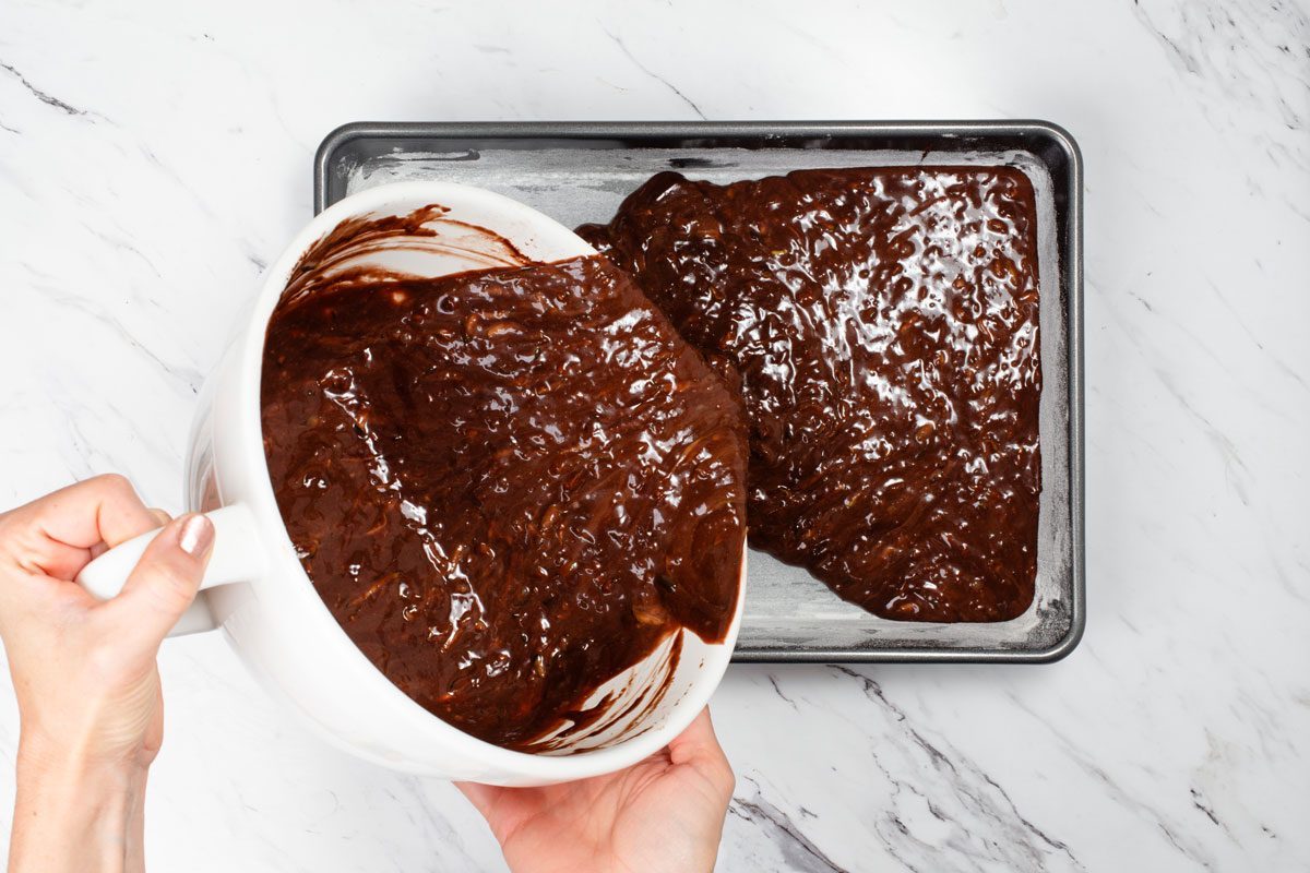 hands pouring Chocolate Zucchini Cake batter into a baking pan