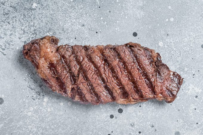 BBQ Grilled denver beef meat steak on a table. Gray background. Top view