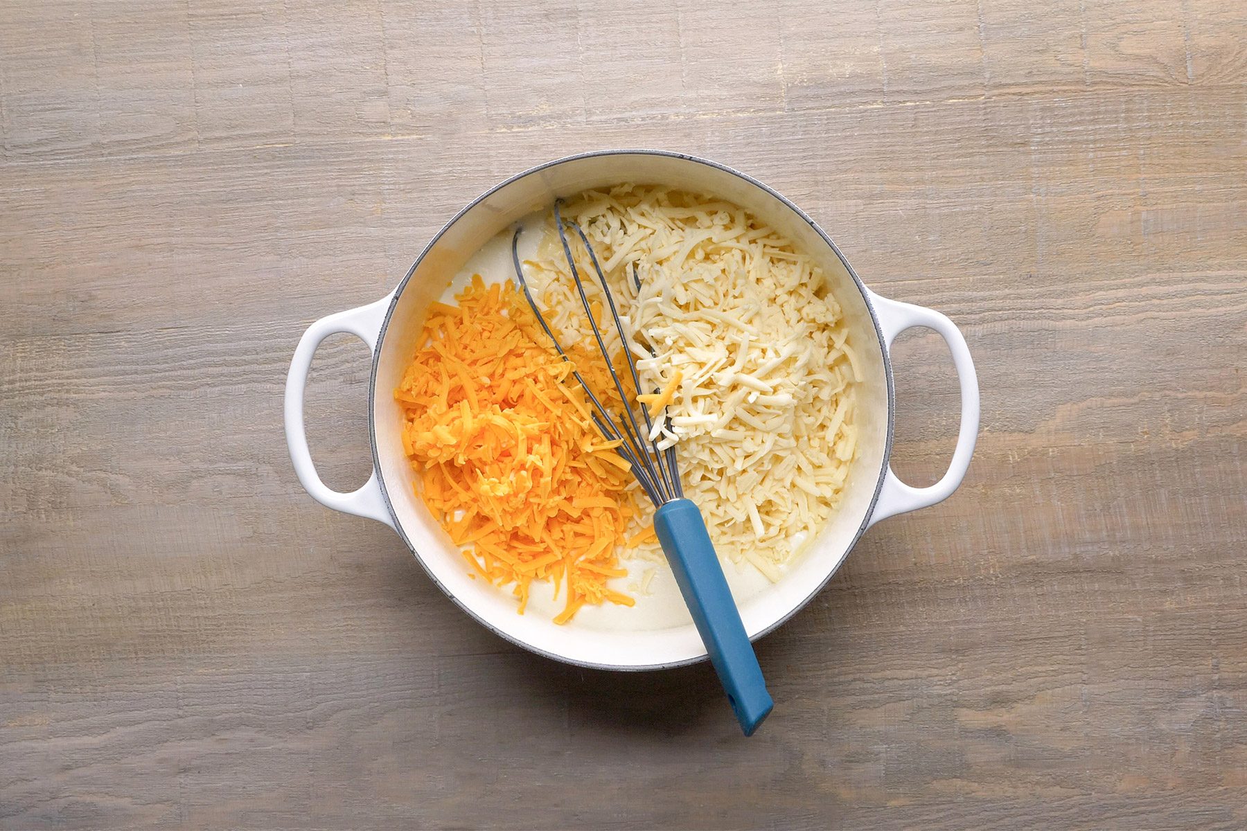 overhead shot; wooden background; grated cheese in a pan with whisker;
