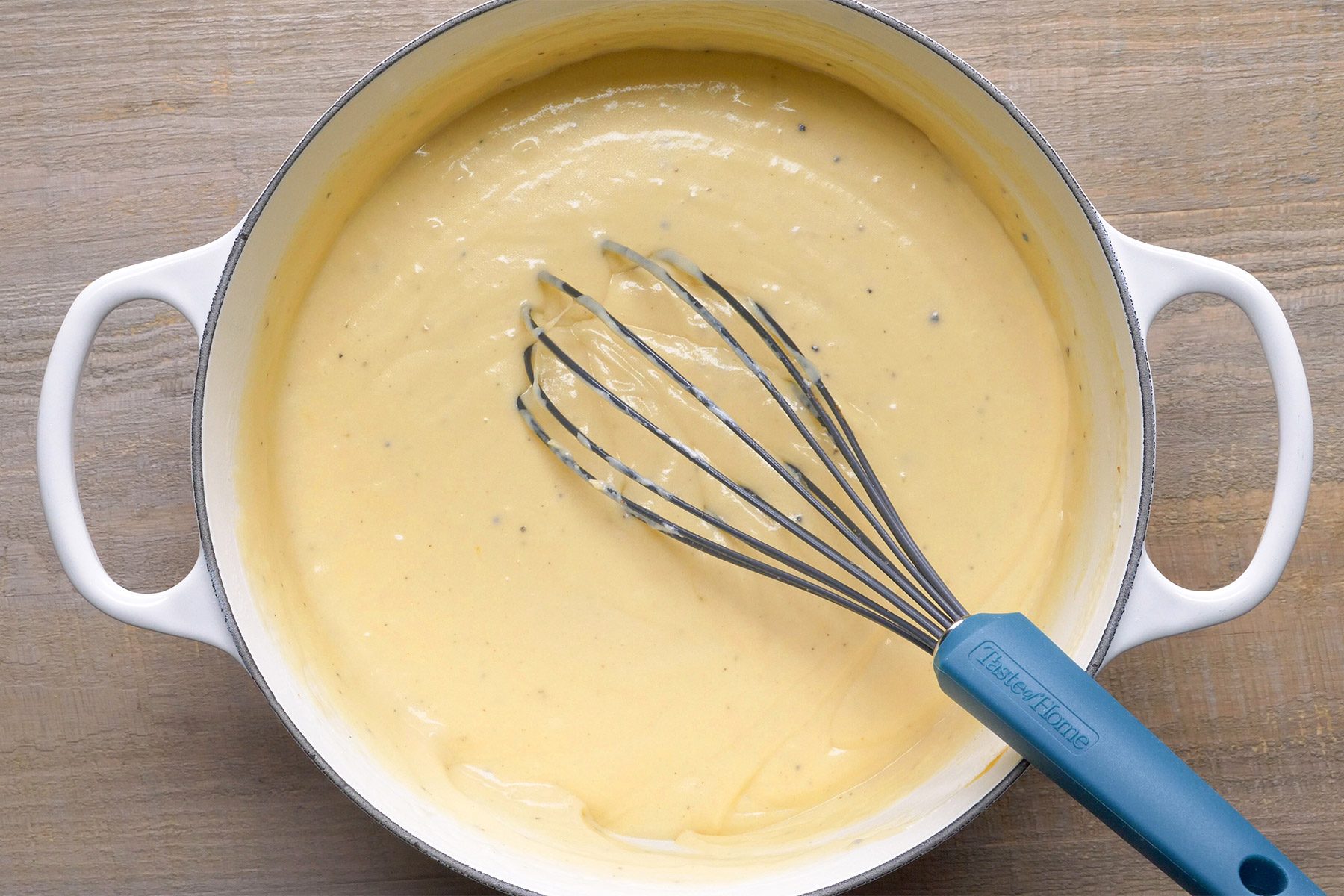 overhead shot; wooden background; melted cheese mixture in a pan with whisker;