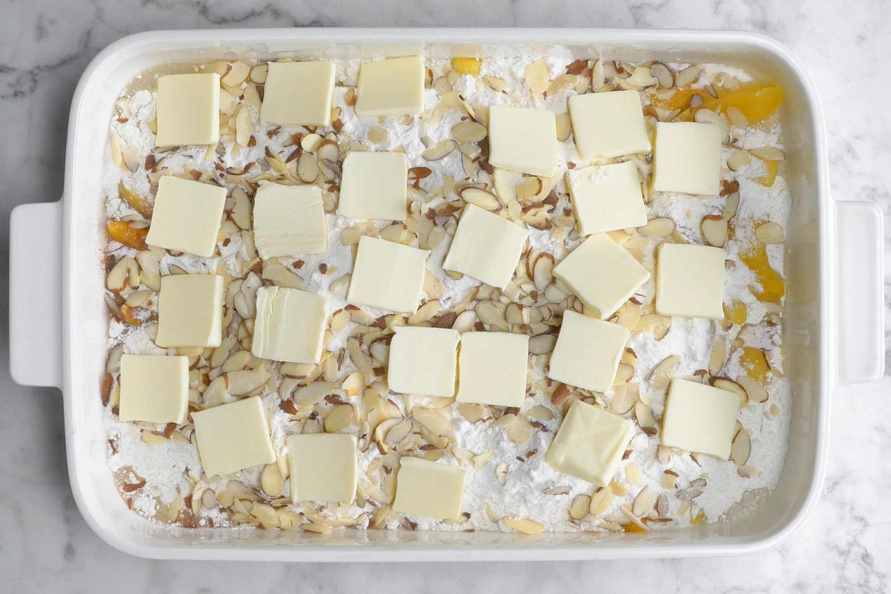 A baking dish layered with cake mix, almonds, and squares of butter