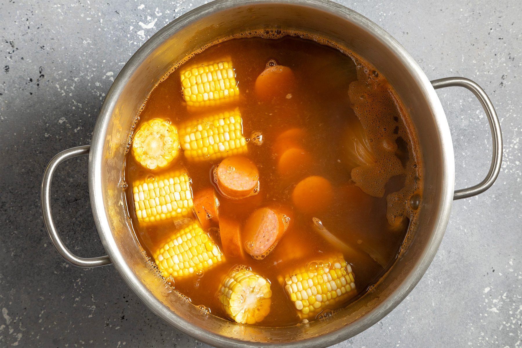 overhead shot of sweet corn and sausages added in the mix in a stockpot