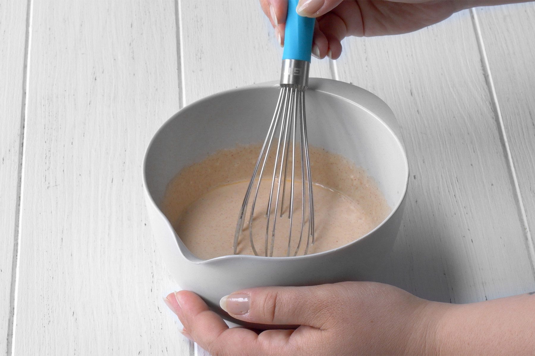 3/4th shot; white background; mixing ingredients in a small bowl with whisker