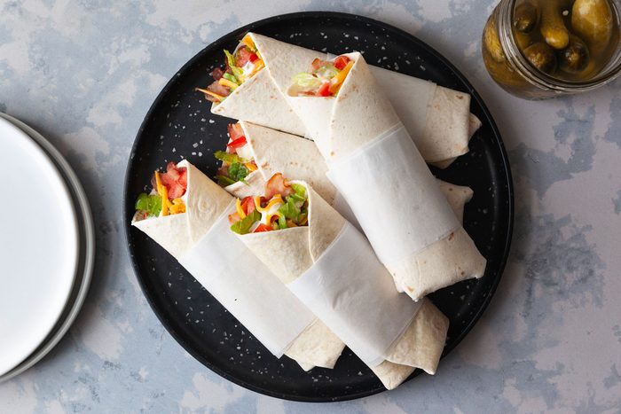 Taste of Home BLT Wraps on a black serving platter with a jar a pickles