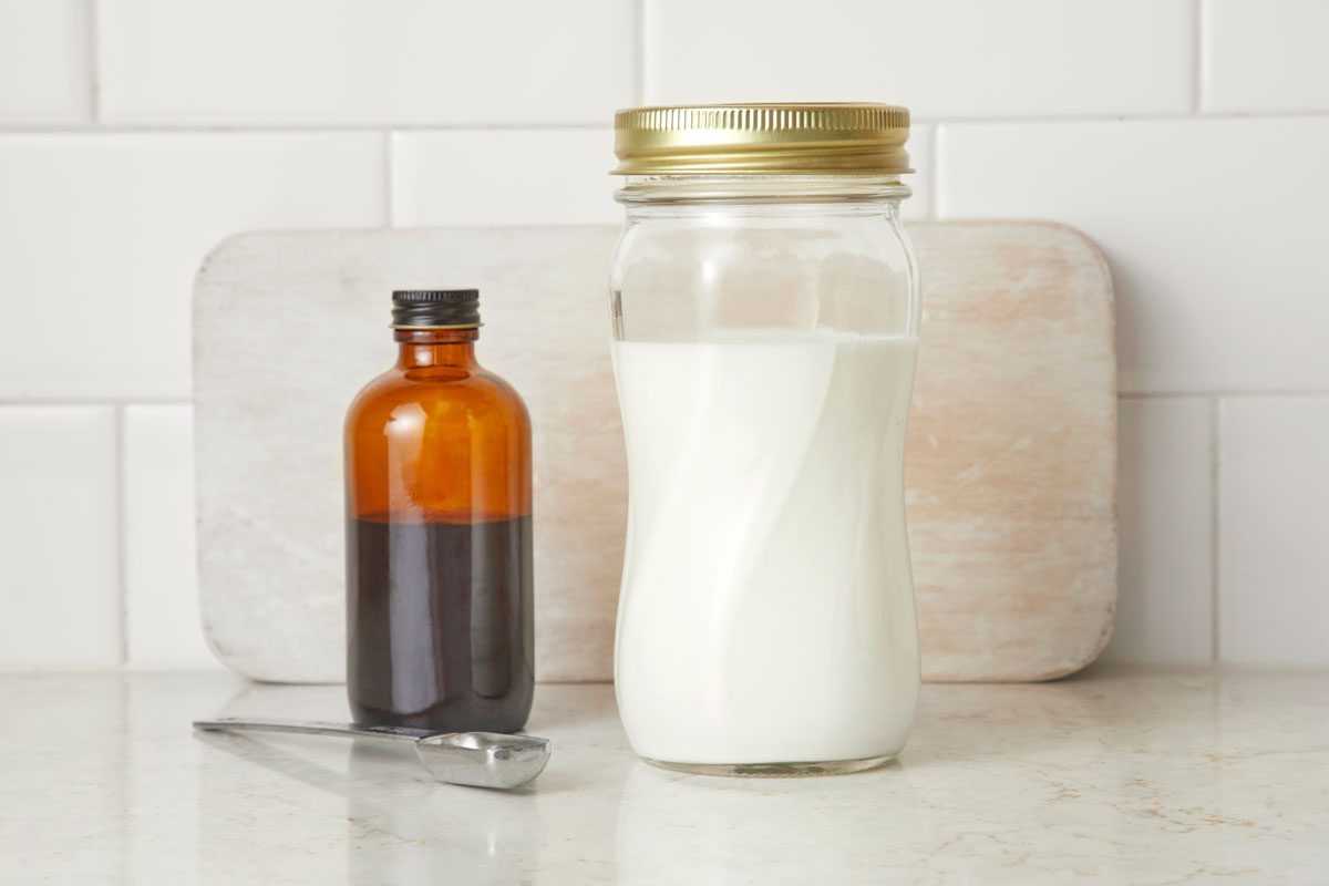 Cream in a glass jar on a kitchen counter with jar of vanilla extract and measuring spoon nearby