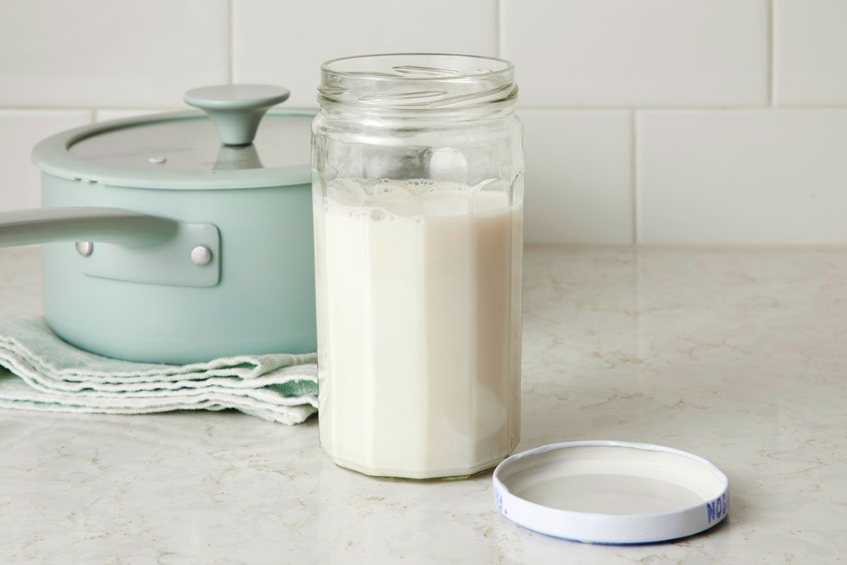 Nut milk in a glass jar on a kitchen counter with saucepan in the background nearby