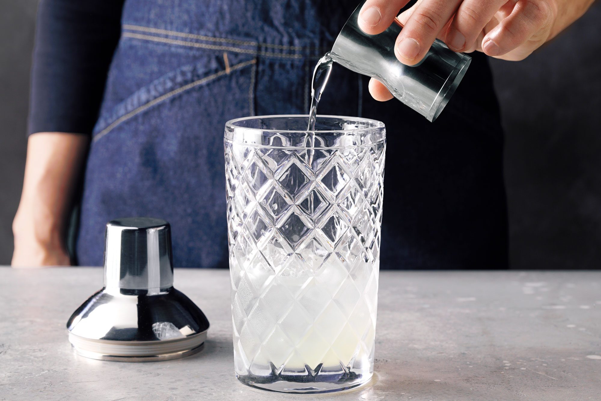 Table view shot of fill a shaker half full with ice; add gin; lemon juice and syrup; marble background;