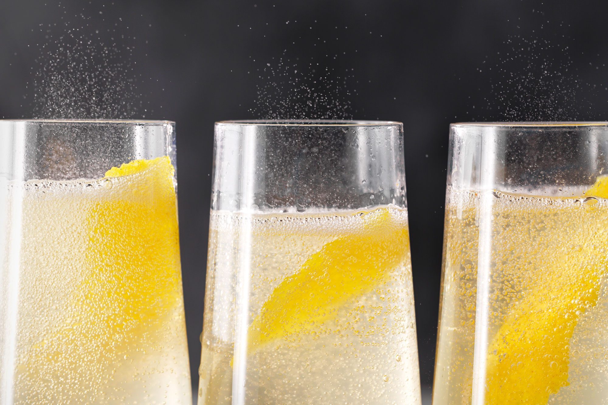 close view shot of French 75 Cocktail; served in three champagne glasses; garnished with lemon peel; marble background;