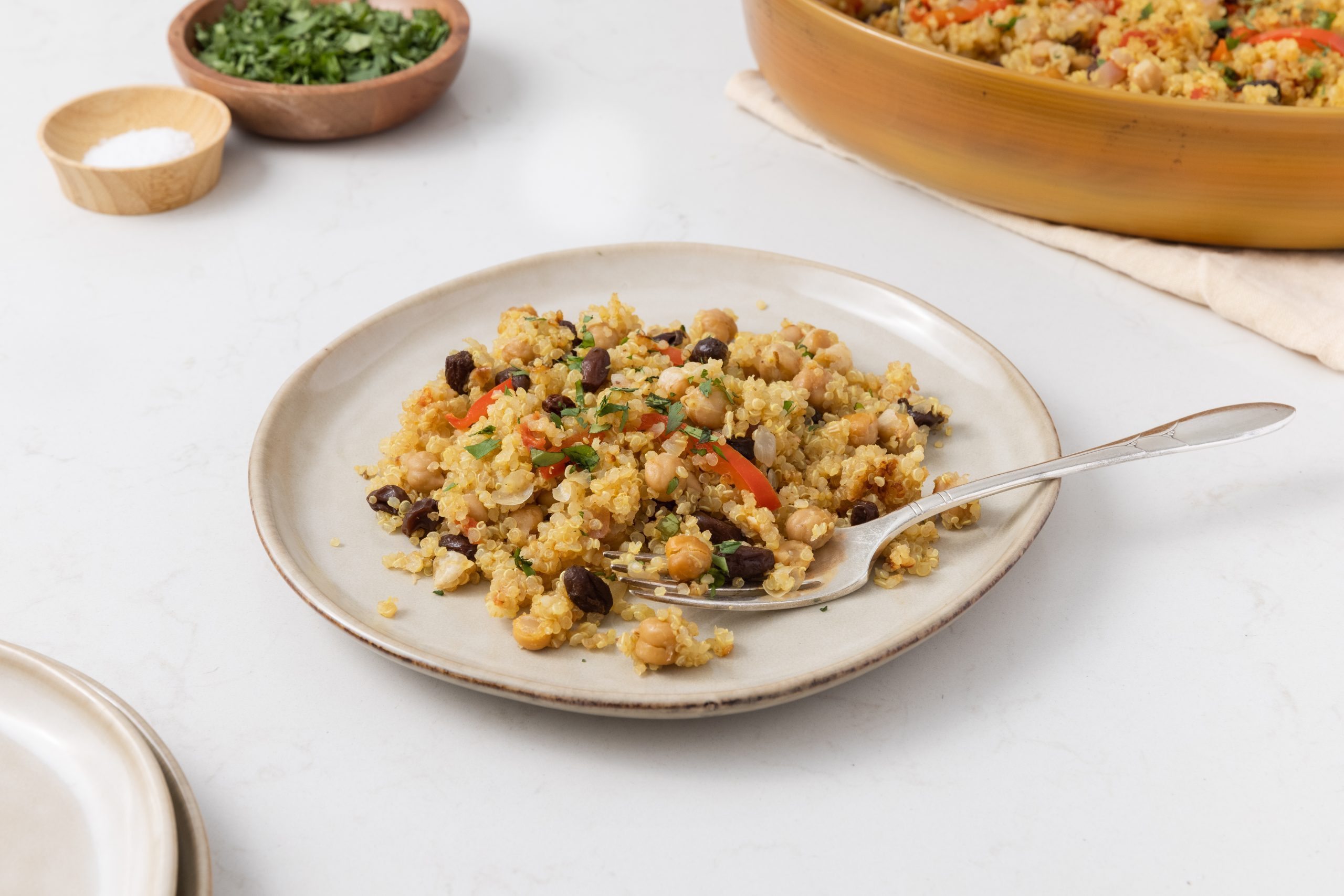 Close up of quinoa chickpea salad on plate with fork and serving dish in the background.