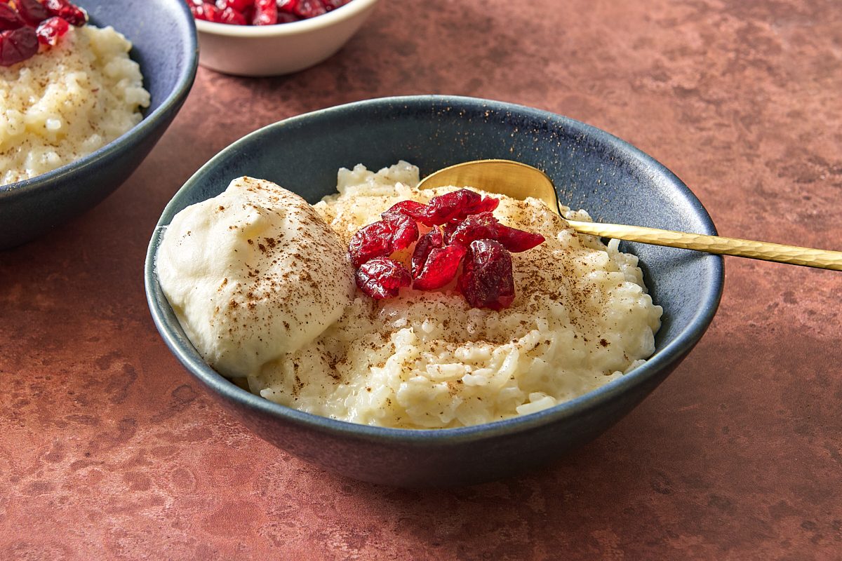 Closeup of a bowl of rice pudding with leftover rice, topped with cinnamon, whipped cream and dried cranberries