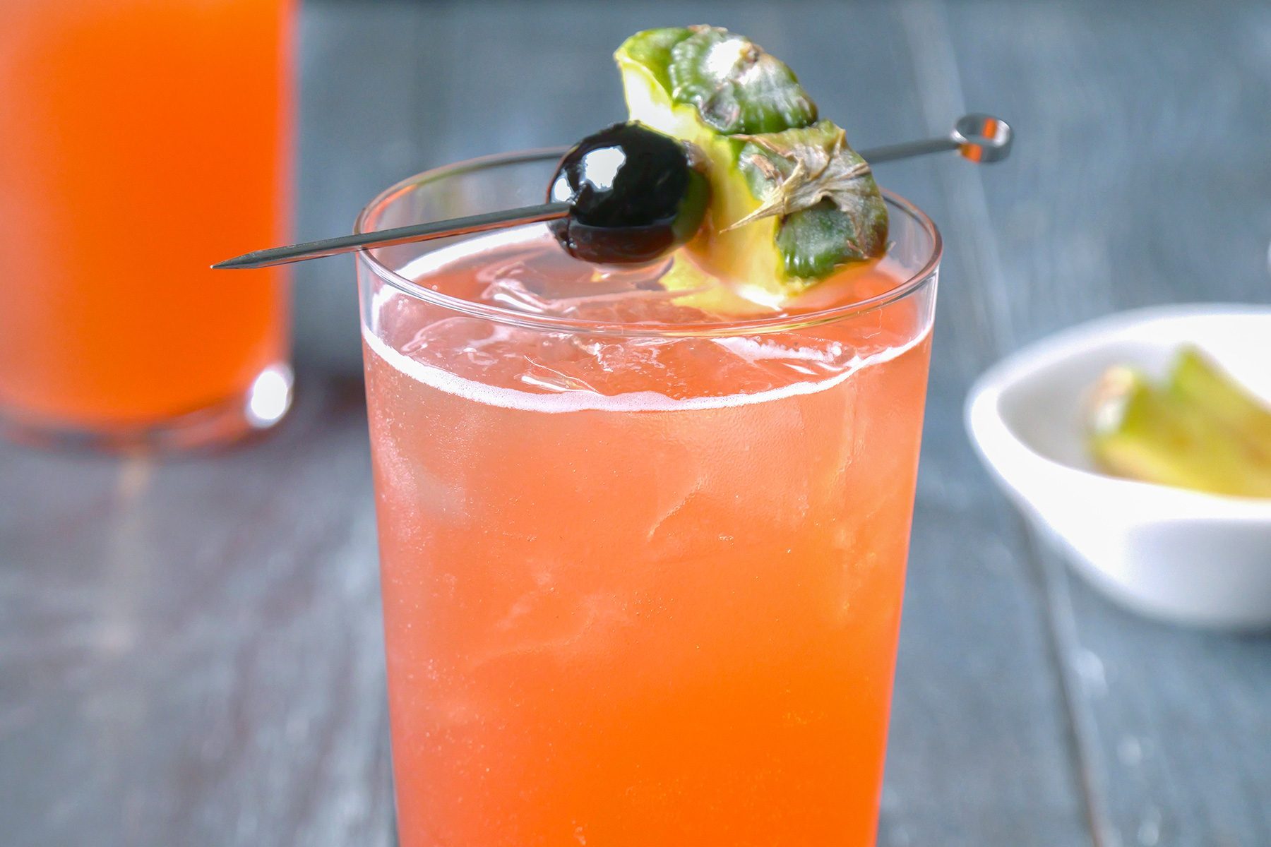 horizontal shot; wooden background; Singapore Sling served into chilled sling glass; top with club soda; Garnish with cherries;