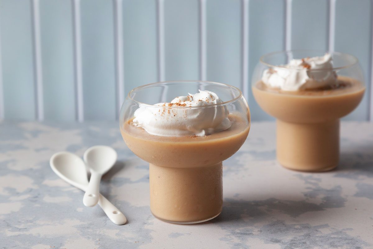 Two single servings of Butterscoth pudding with whipped cream and ground nutmeg in dessert dishes with white spoons