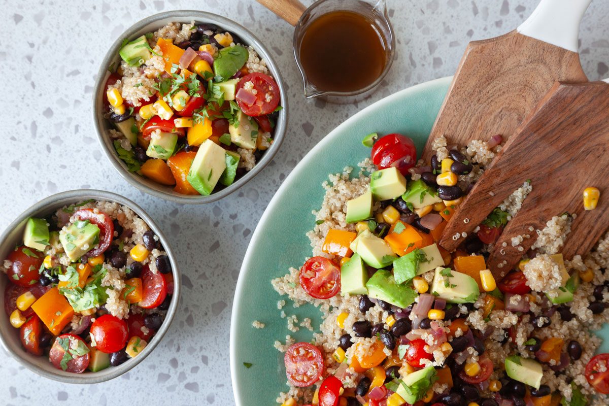 Southwest Quinoa Salad in an aqua serving bowl with wooden salad hands and two single servings 