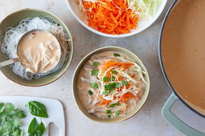 Coconut curry chicken soup in green bouls with carrot and cabbage garnish, basil and cilantro on a cutting board,
