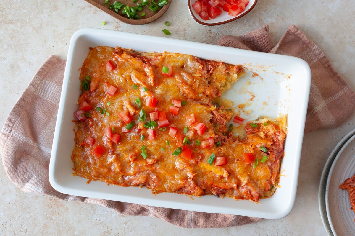 13x9 baking dish with Chicken Tamale Bake garnished with tomato and green onions, with a scoop out.