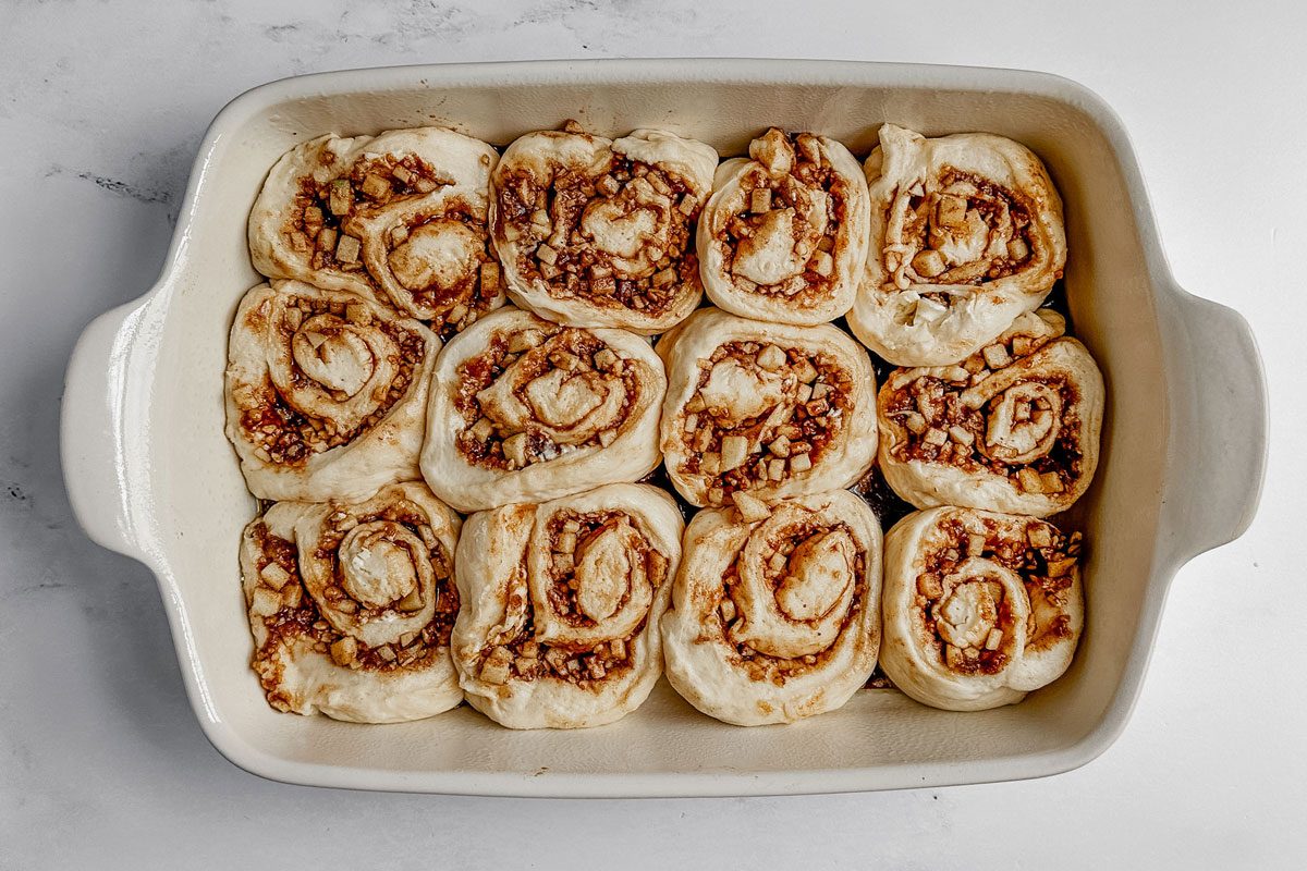Unbaked Taste of Home apple cinnamon rolls in a white baking dish on a marble surface.