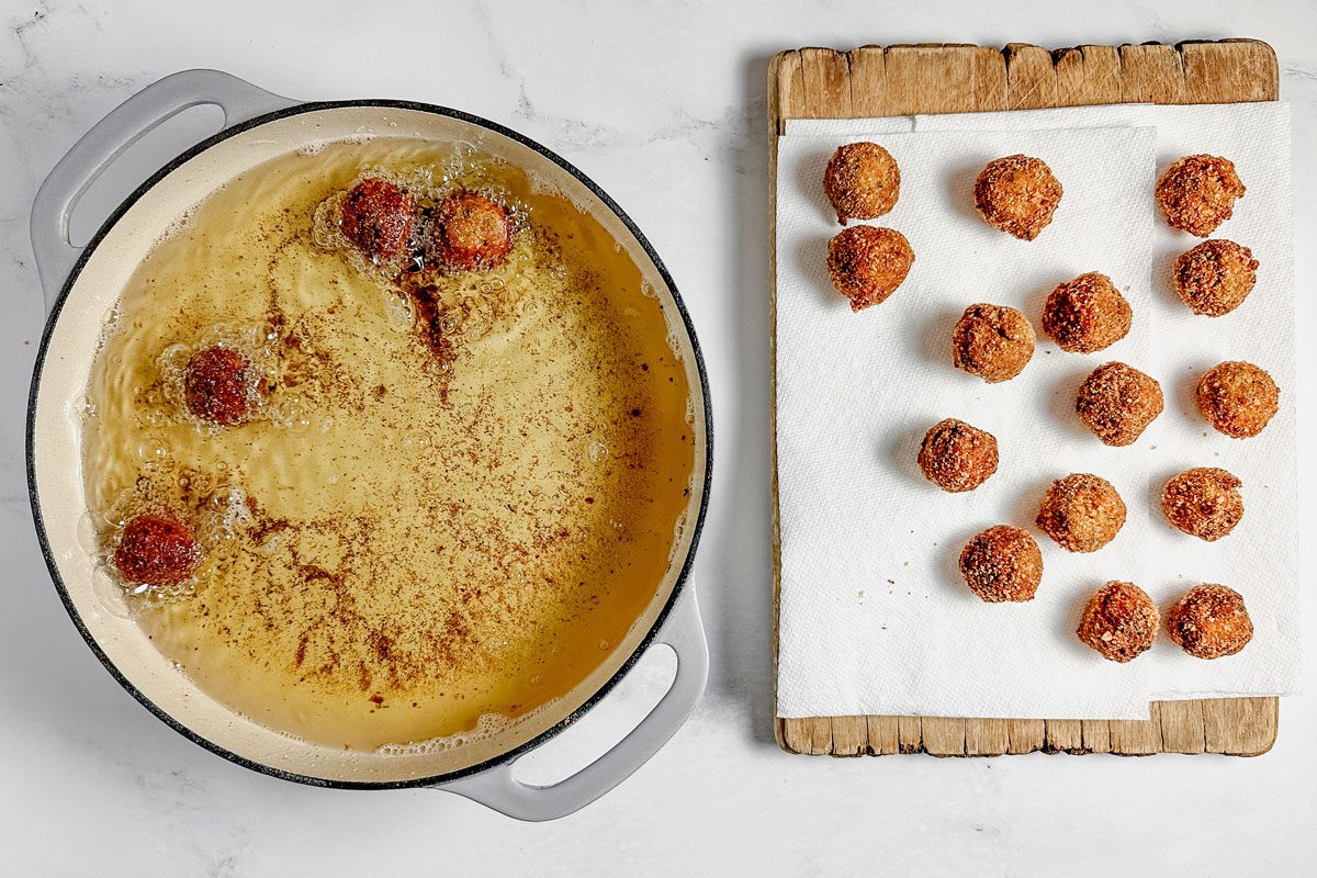 Taste of Home Bitterballen in a skillet next to drained Bitterballen on paper towels on a marble surface.